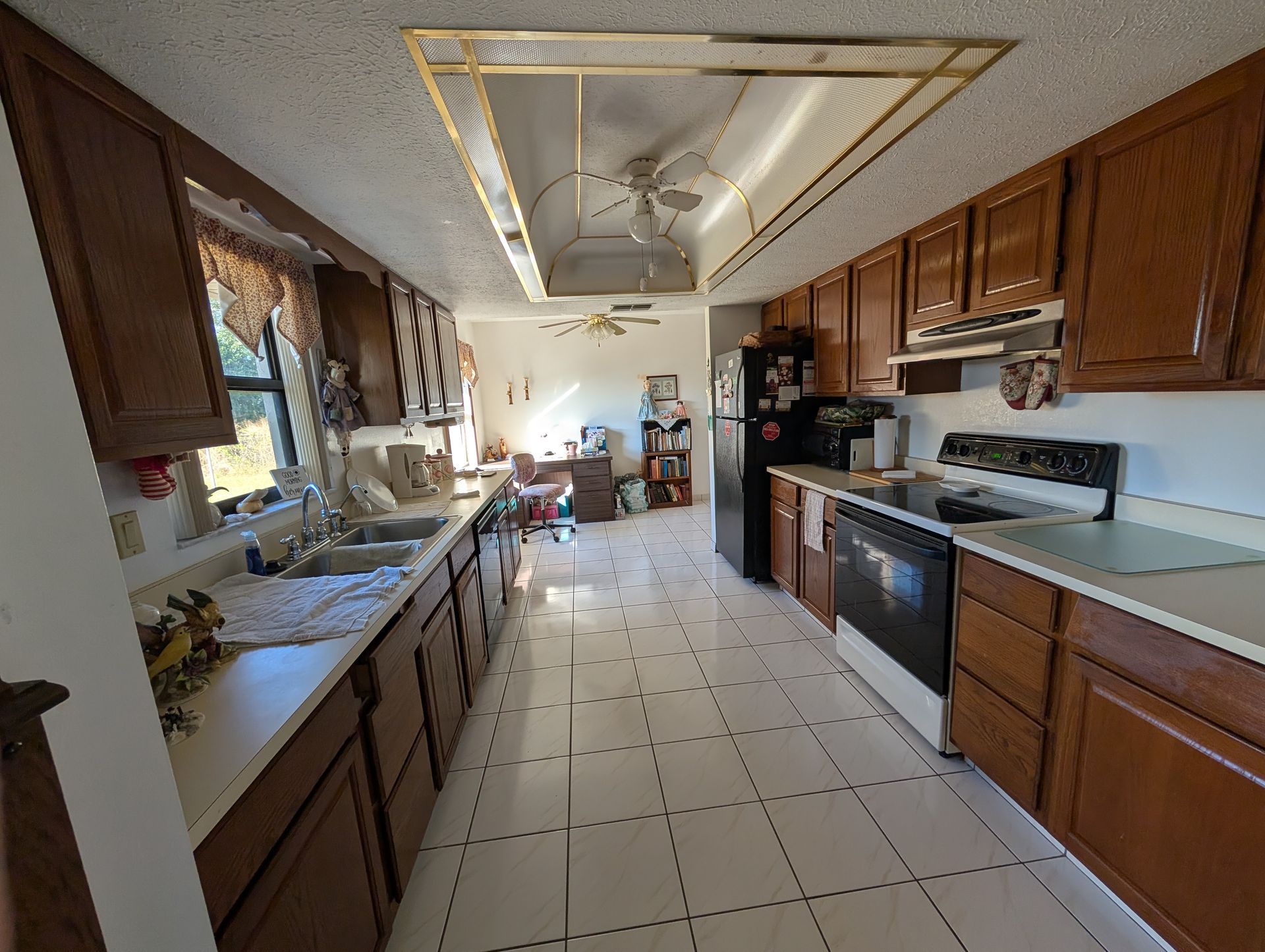 Long, narrow kitchen with brown cabinets, white countertops, and black appliances.
