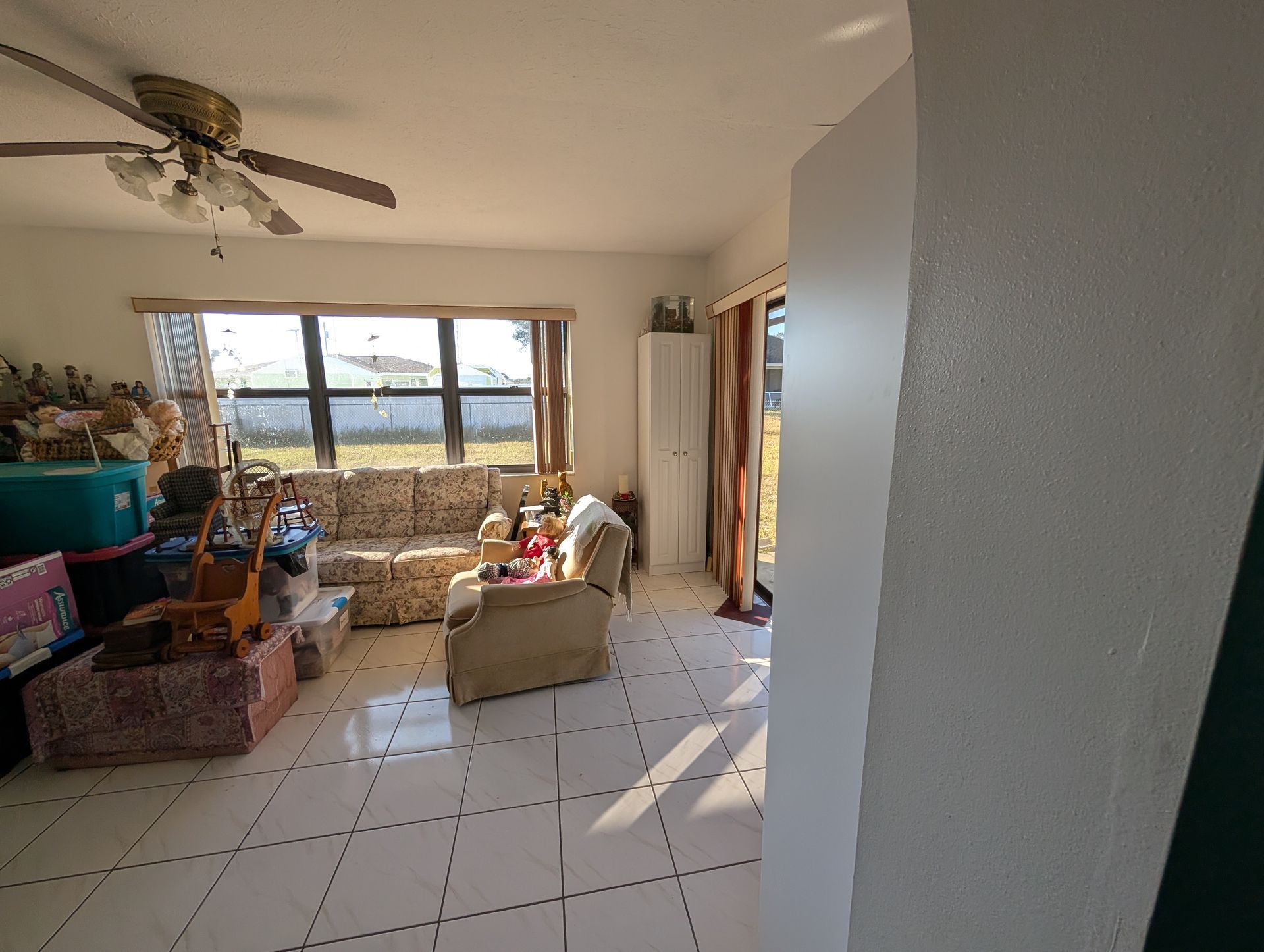 Bright living room with tile floor, sofa, chair, window, storage containers, ceiling fan, and white storage cabinet.