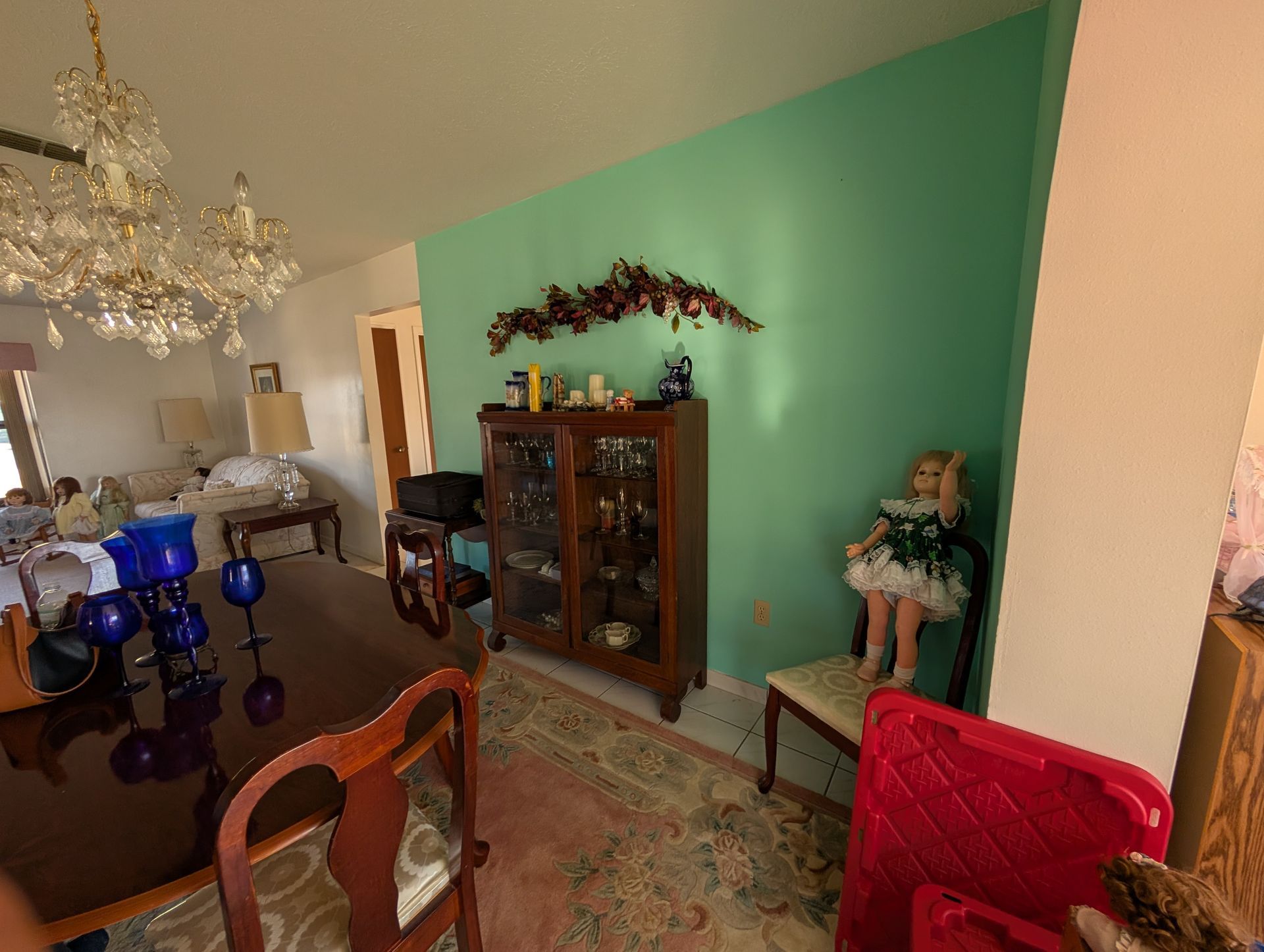 Dining room with a chandelier, wooden cabinet, and doll next to an aqua wall.