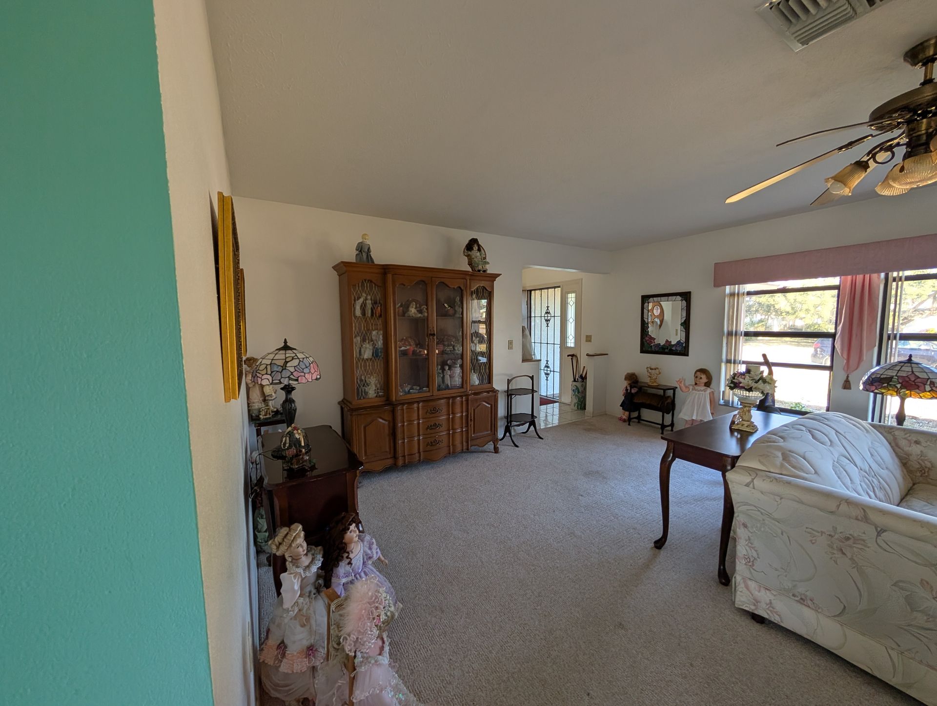Living room with wooden cabinet, sofa, small table, dolls, and a young person.