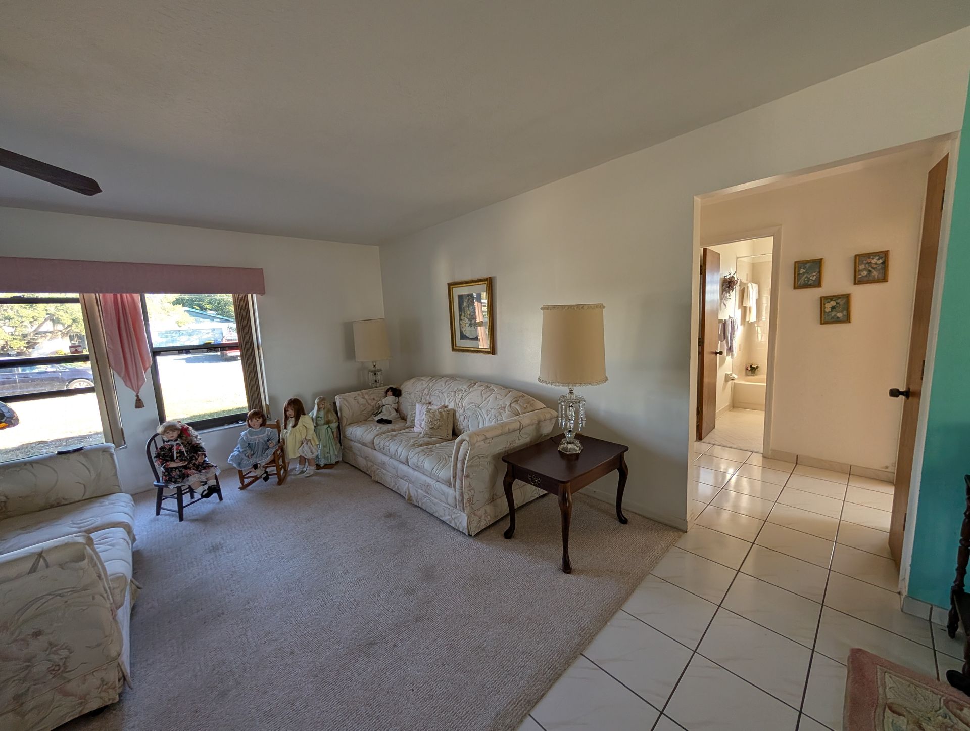 Living room with sofa, chairs, dolls, lamps, and a view into a hallway and bathroom.