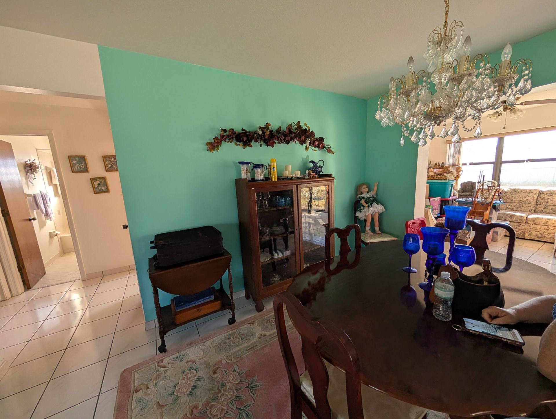 Dining room with teal wall, chandelier, and a table set for eating.