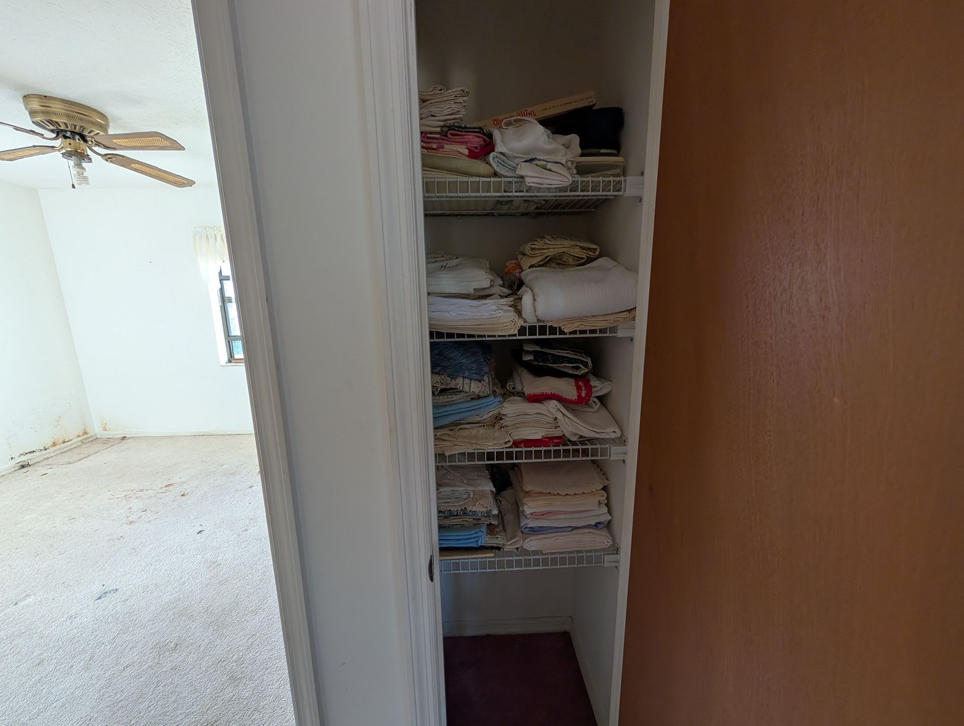 Open closet with wire shelves holding folded linens; bedroom visible.