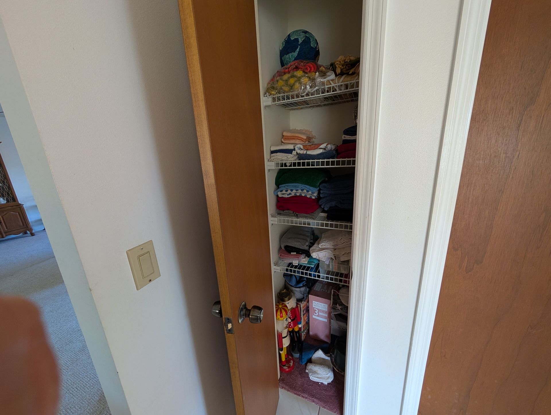 A narrow closet with wire shelves is open, filled with folded clothes and toiletries.