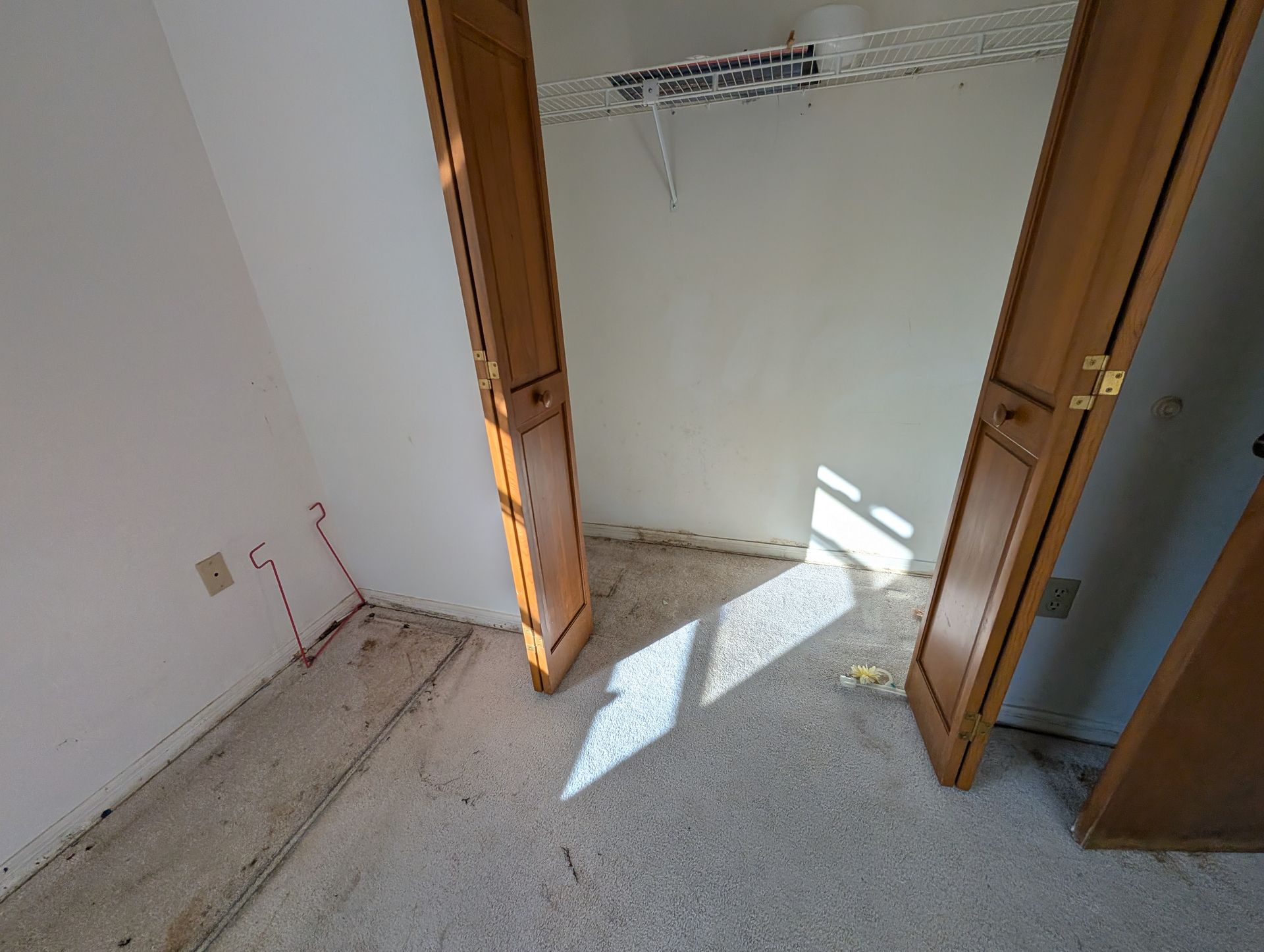 Empty closet with open wooden doors, white walls, and speckled floor.