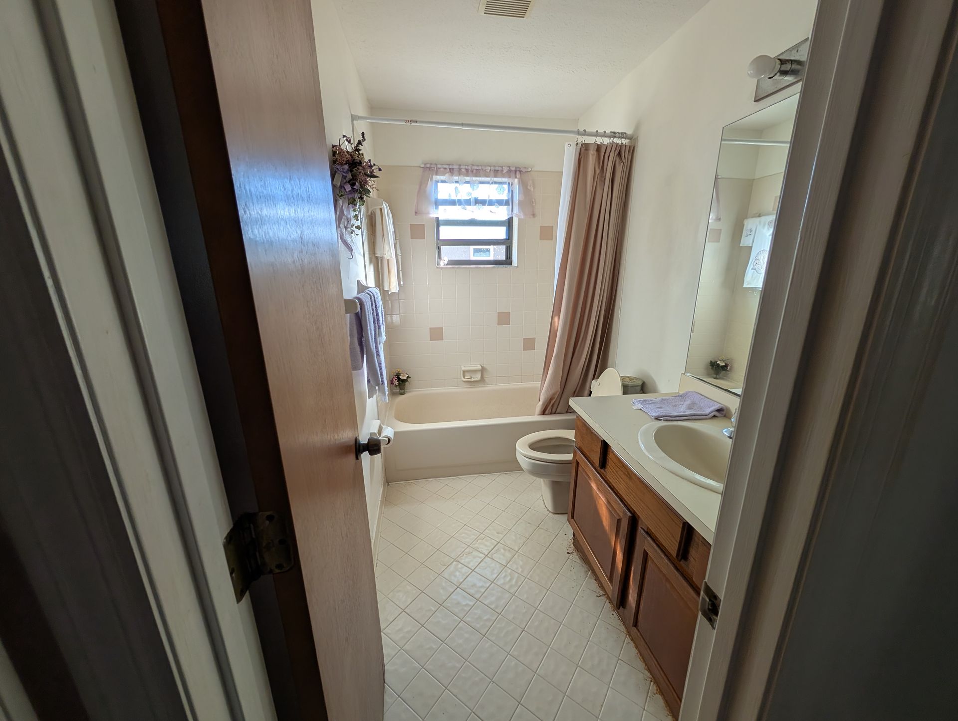 Bathroom interior with white walls, beige tile, and a brown vanity. Open doorway reveals the space.