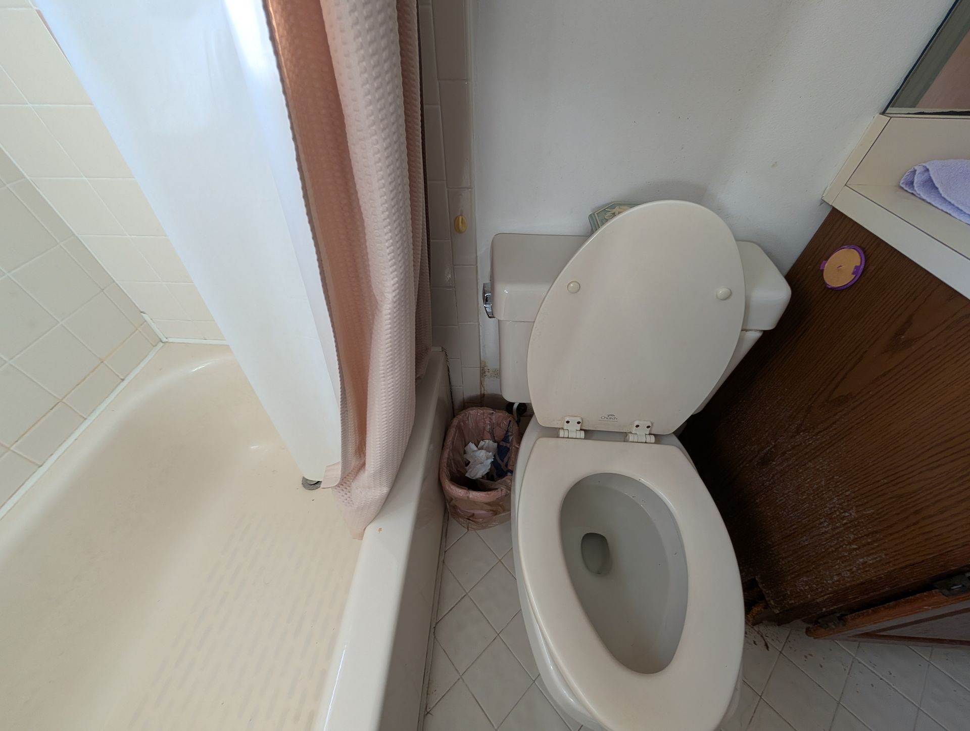 Toilet with the lid up next to a bathroom cabinet and bathtub with a shower curtain.