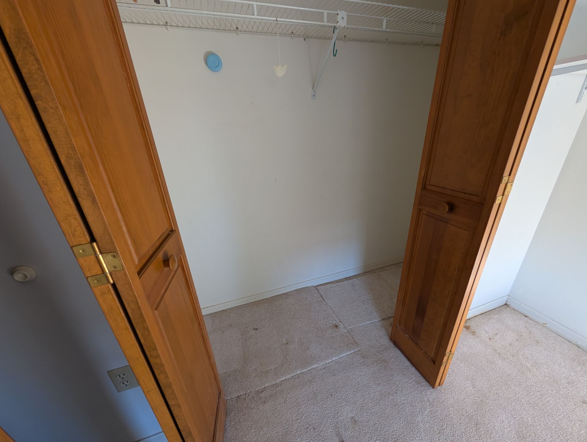 Wooden closet doors open to a mostly empty interior with a clothes rod and carpet.