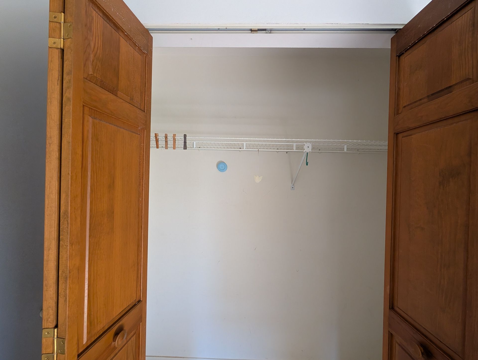 Open, empty closet with wooden doors and a wire shelf.