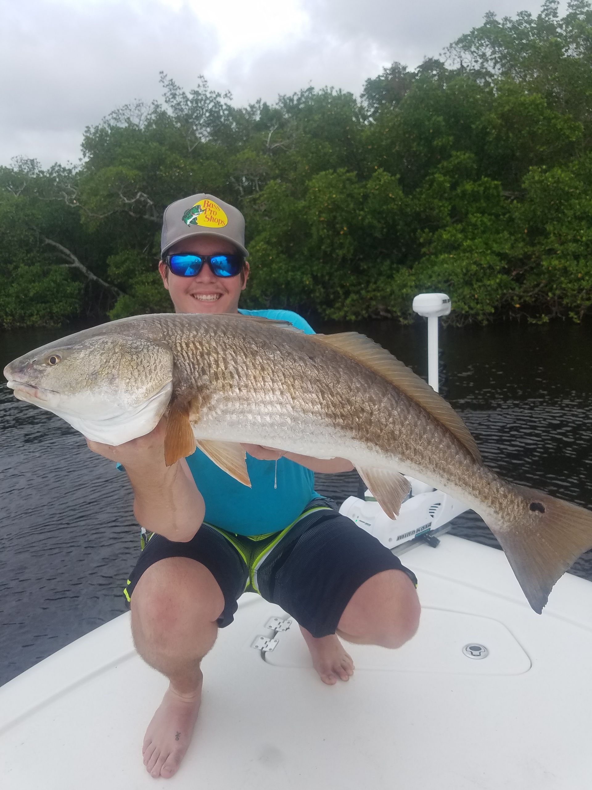 A man is kneeling on a boat holding a large fish.