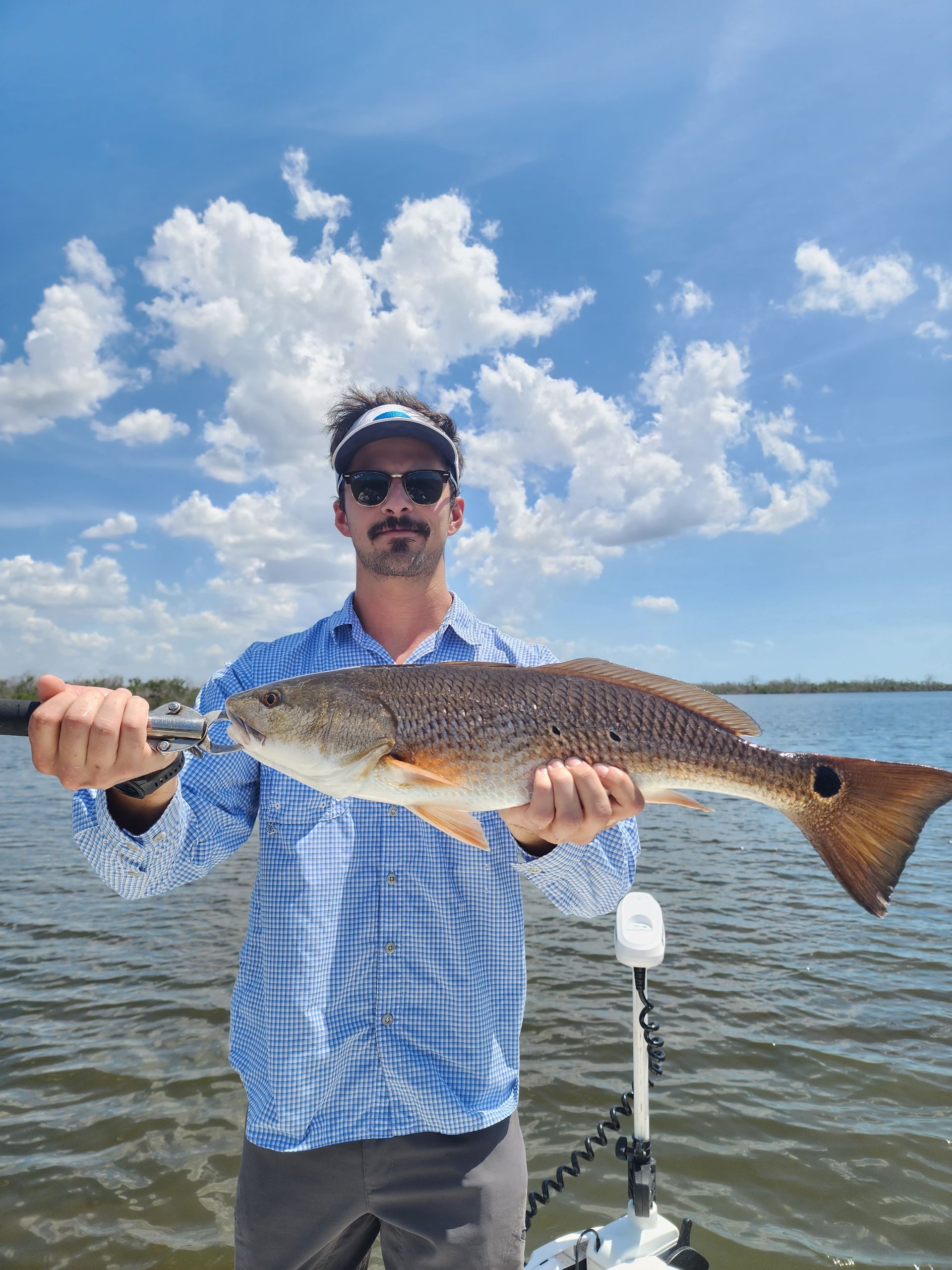 A man is standing on a boat holding a large redfish.