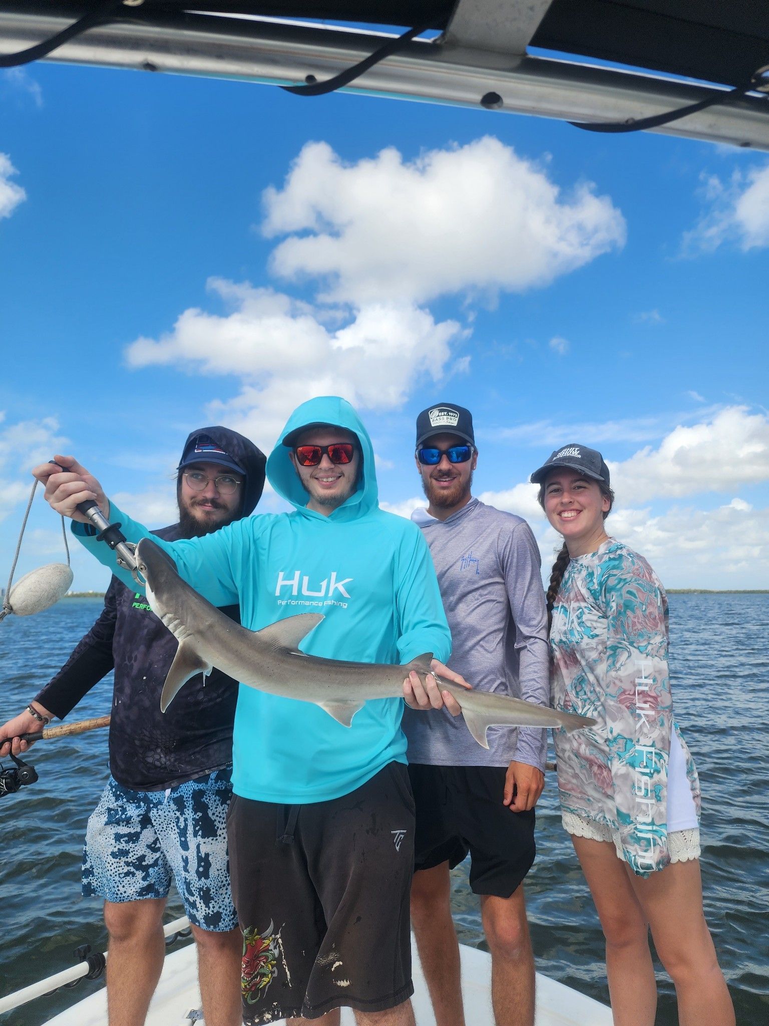 A group of people are standing on a boat holding a shark.