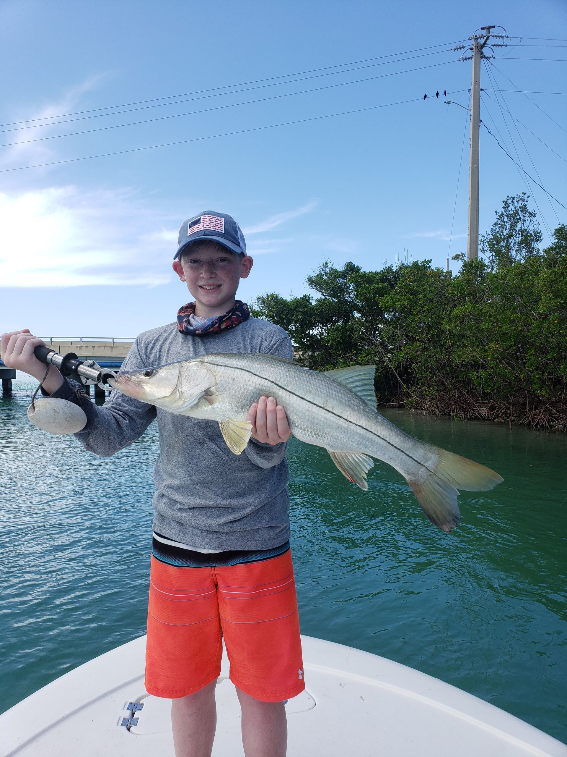 A young man is standing on a boat holding a large fish.