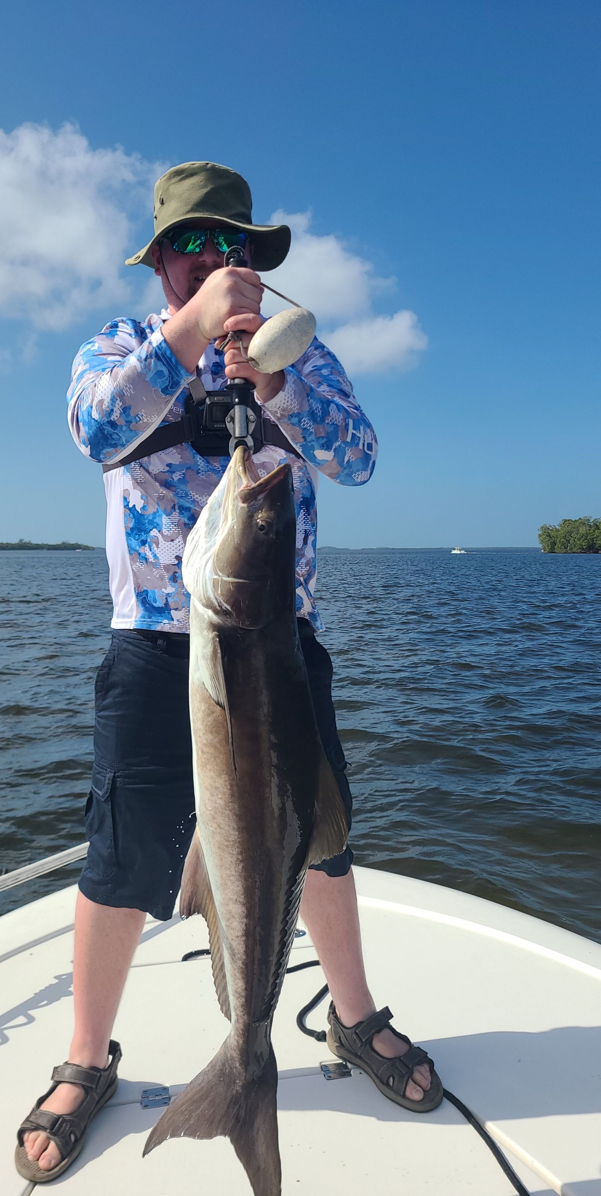 A man is standing on a boat holding a large fish.