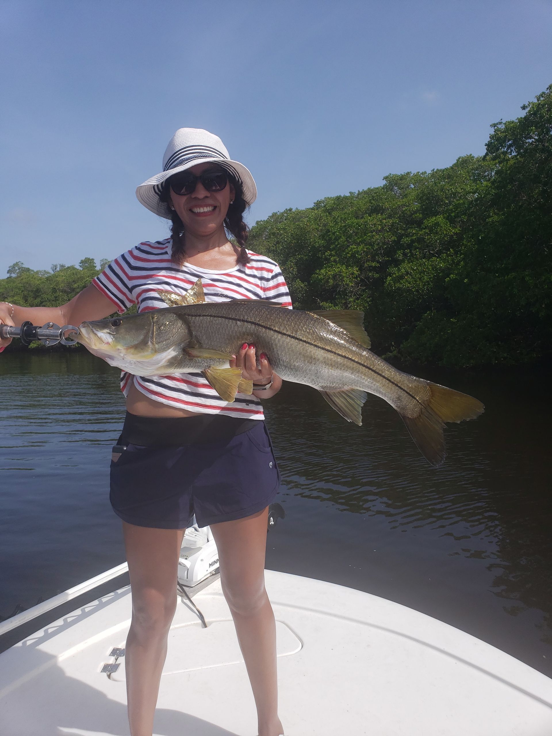A woman is standing on a boat holding a large fish.