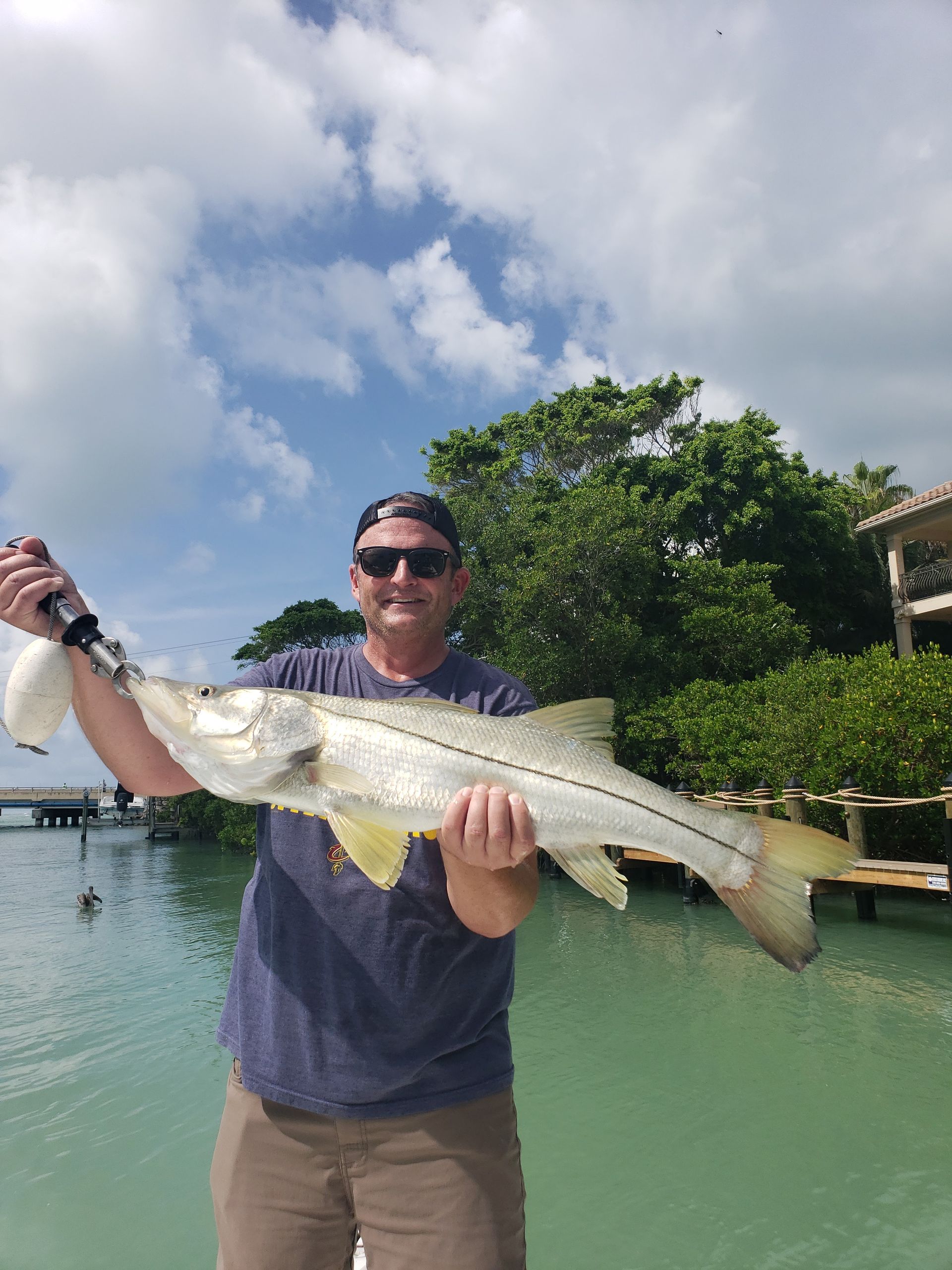 A man is holding a large fish in his hands in front of a body of water.