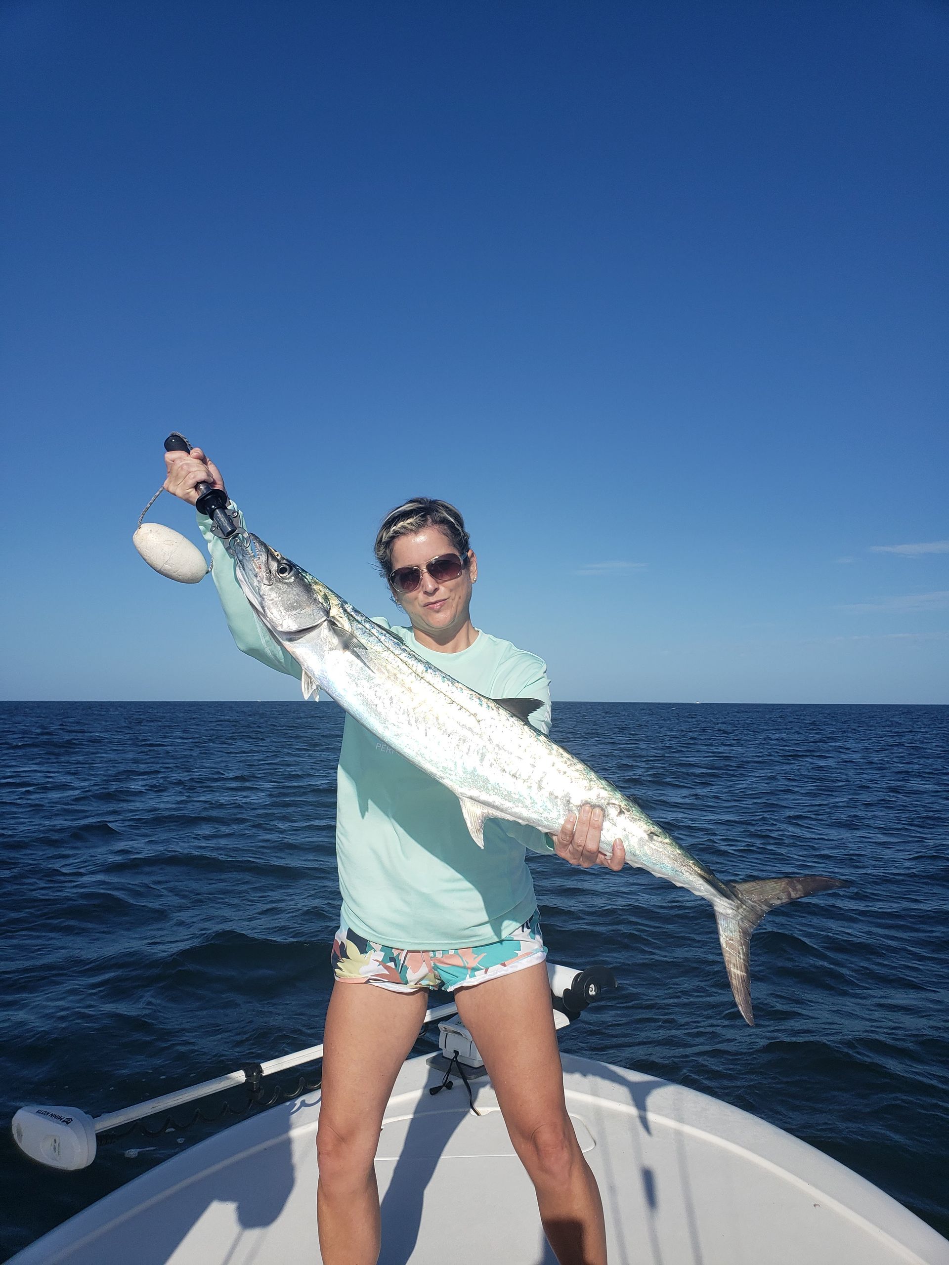 A woman is standing on a boat holding a large fish.