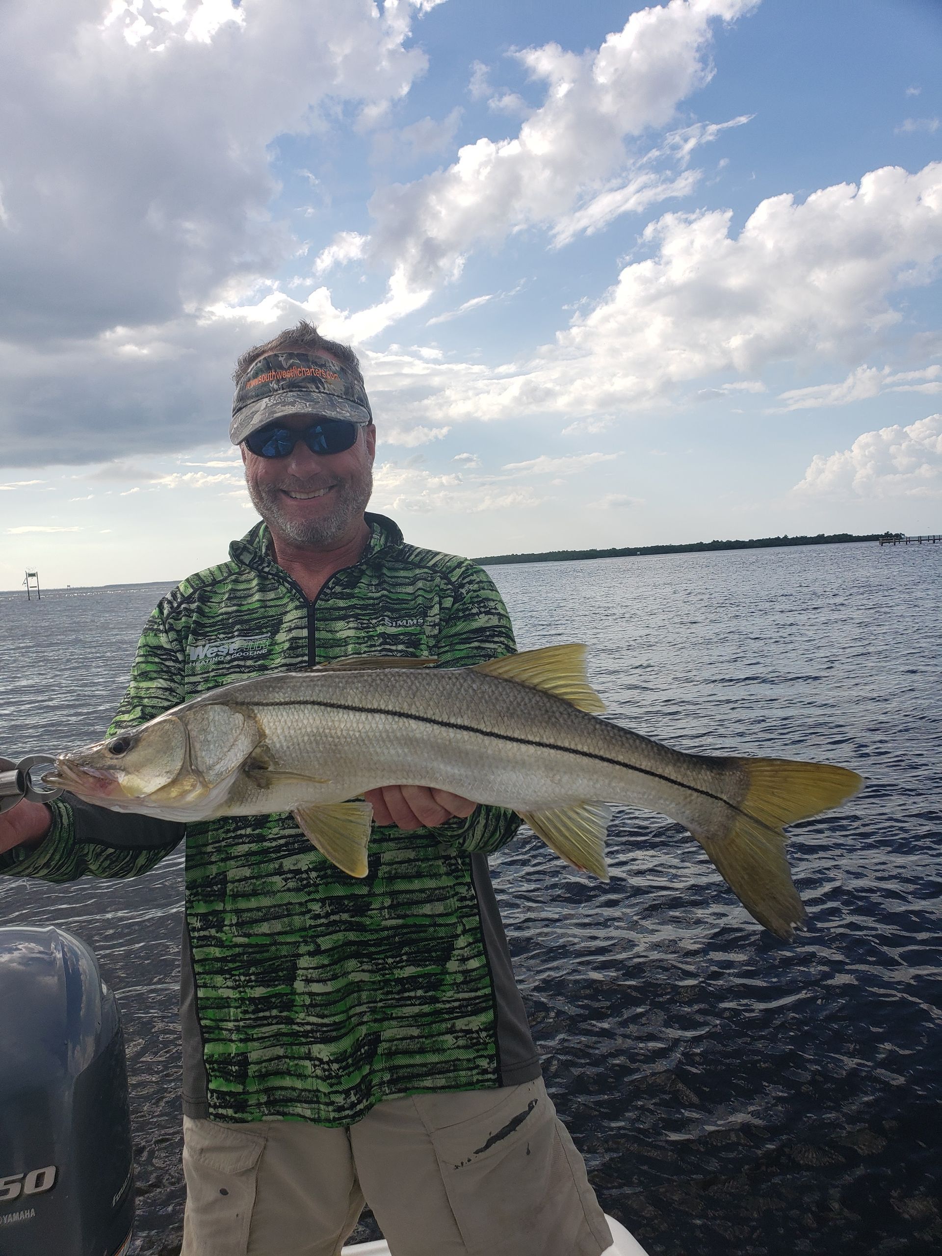 A man is holding a large fish on a boat in the water.