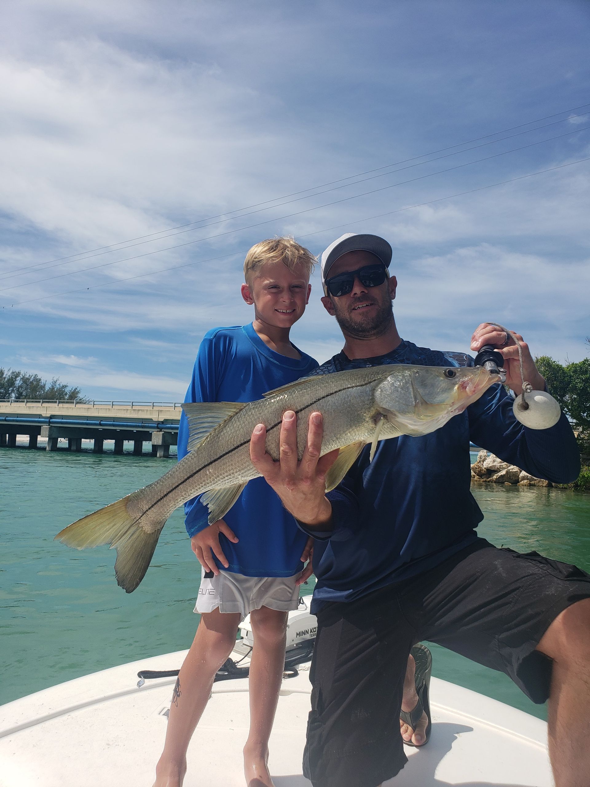 A man and a boy are holding a large fish on a boat.
