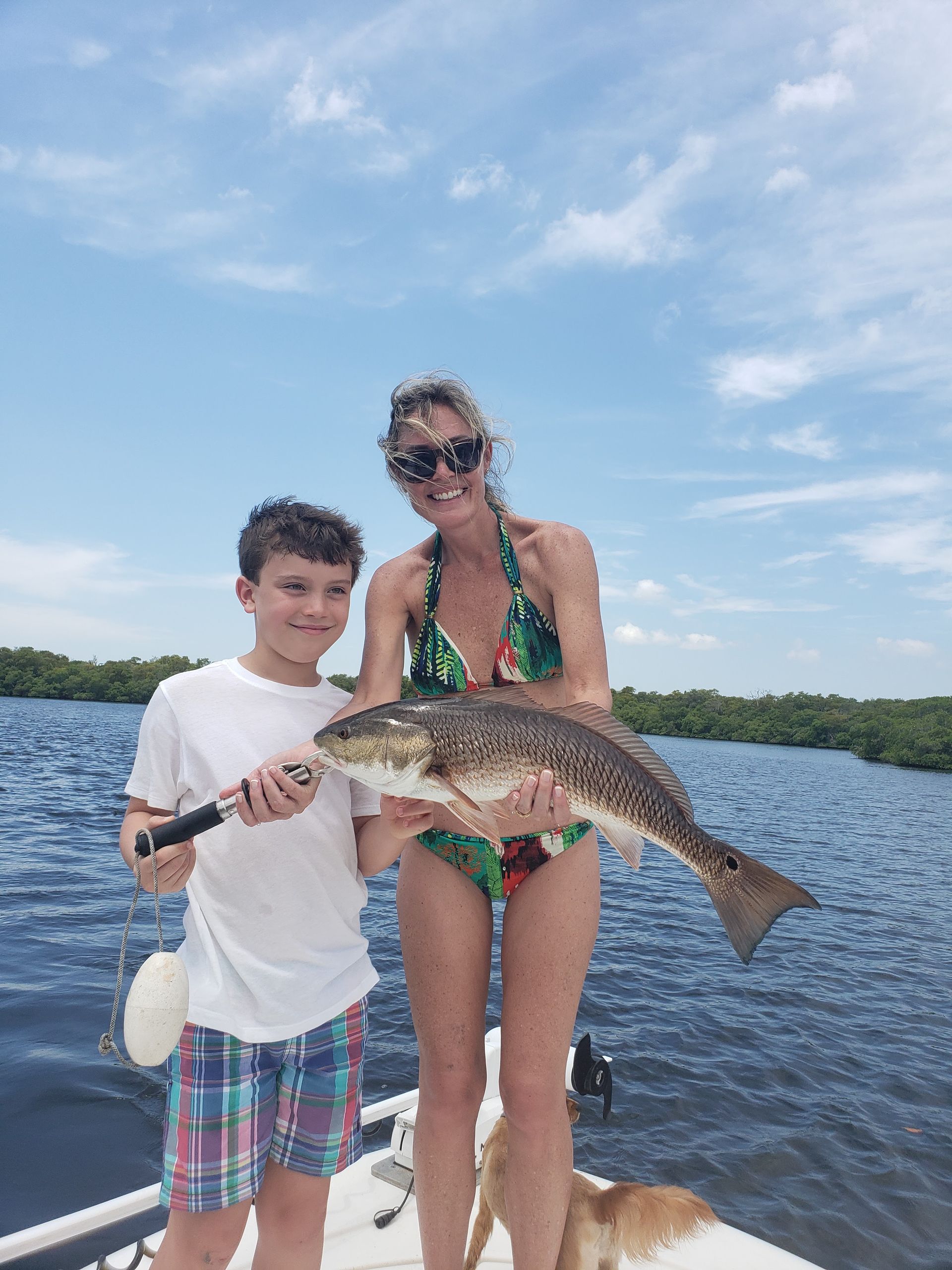 A woman and a boy are holding a large fish on a boat.
