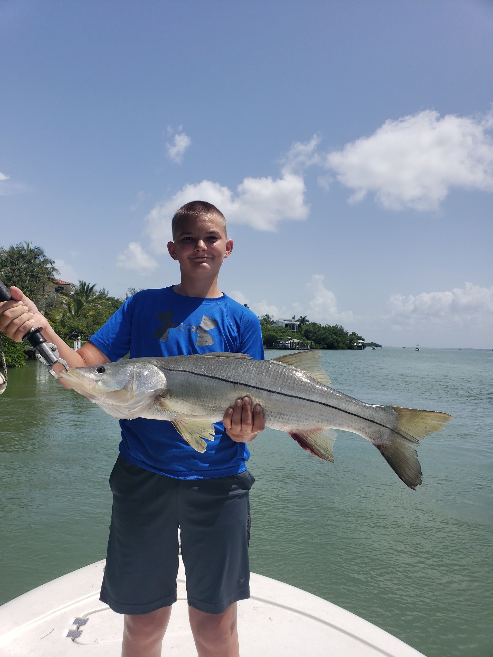 A young man is holding a large fish on a boat.