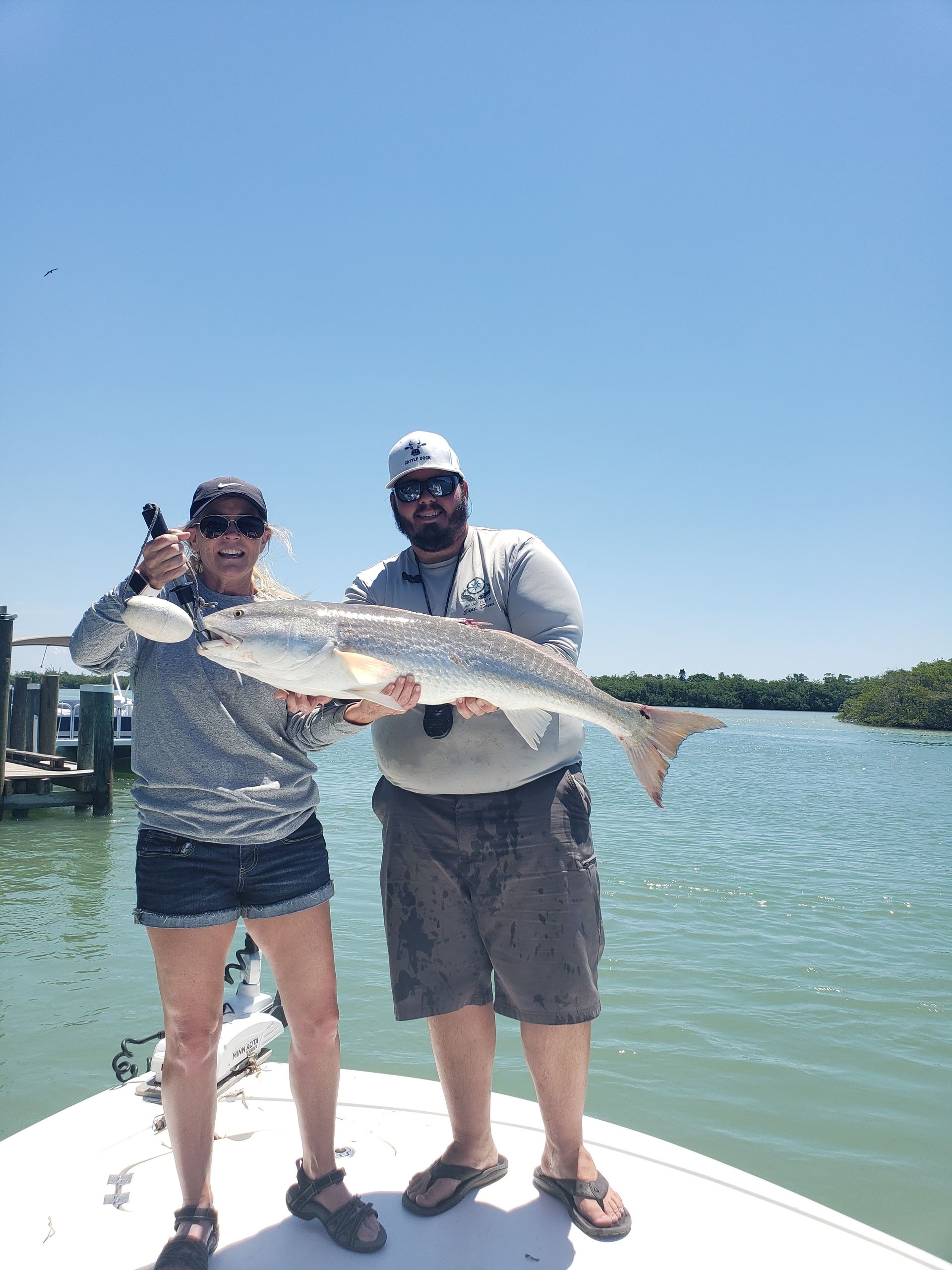 A man and a woman are standing on a boat holding a large fish.