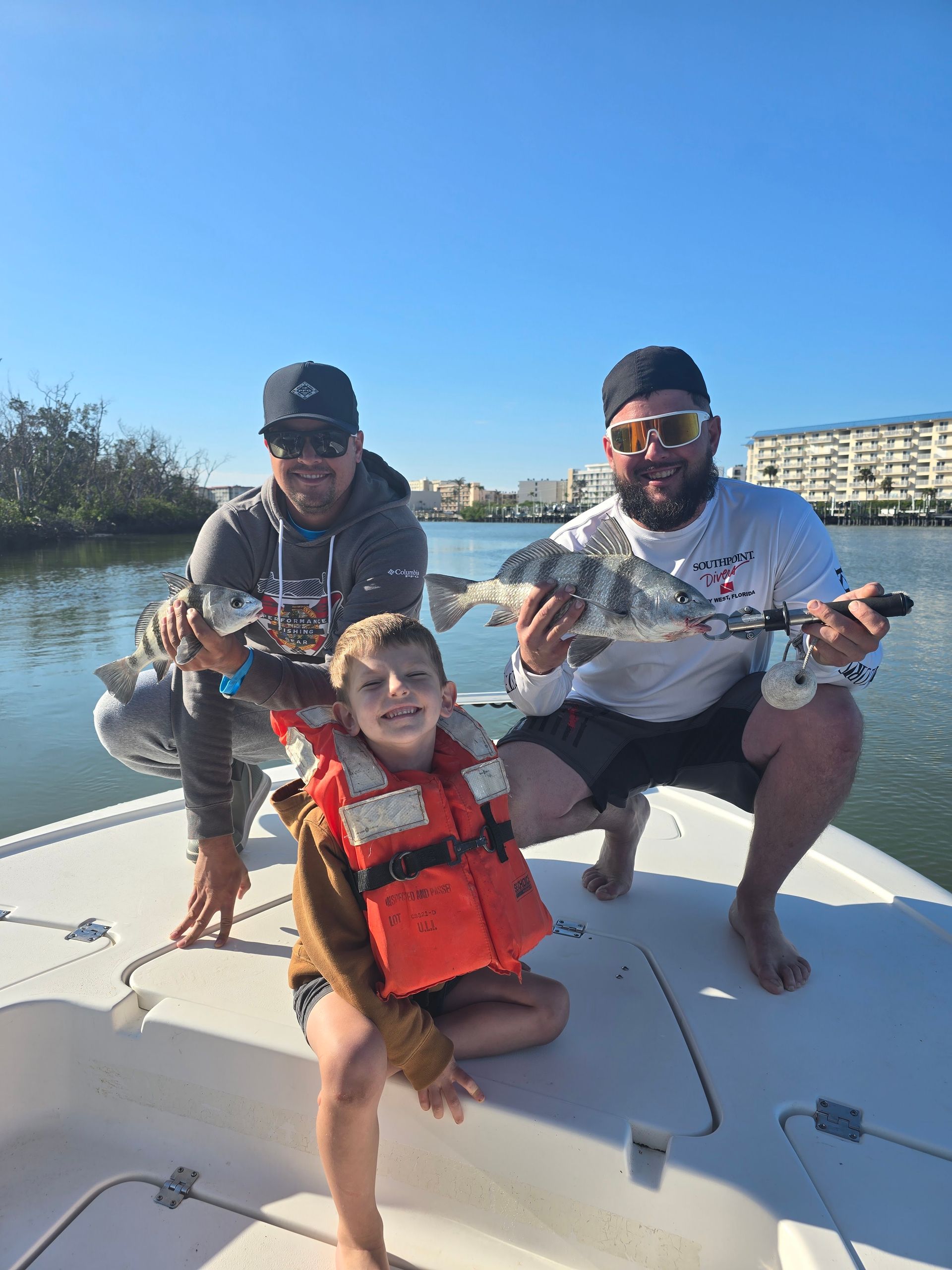 Two men and a little boy are sitting on a boat holding fish.