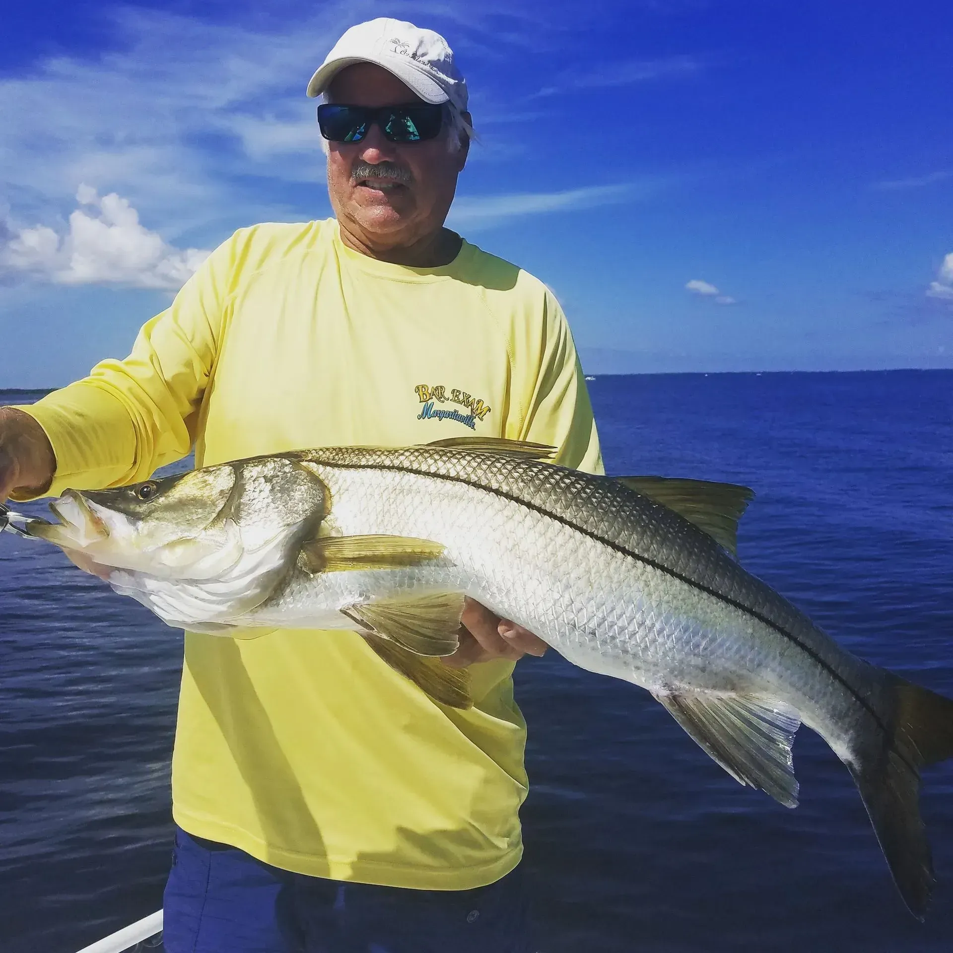 A man in a yellow shirt is holding a large fish in his hands.