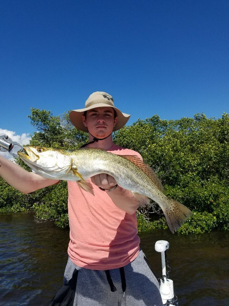 A man in a hat is holding a large fish in his hands.