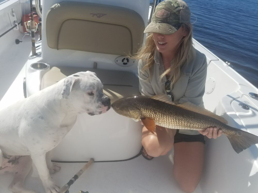A woman and a dog are on a boat holding a fish