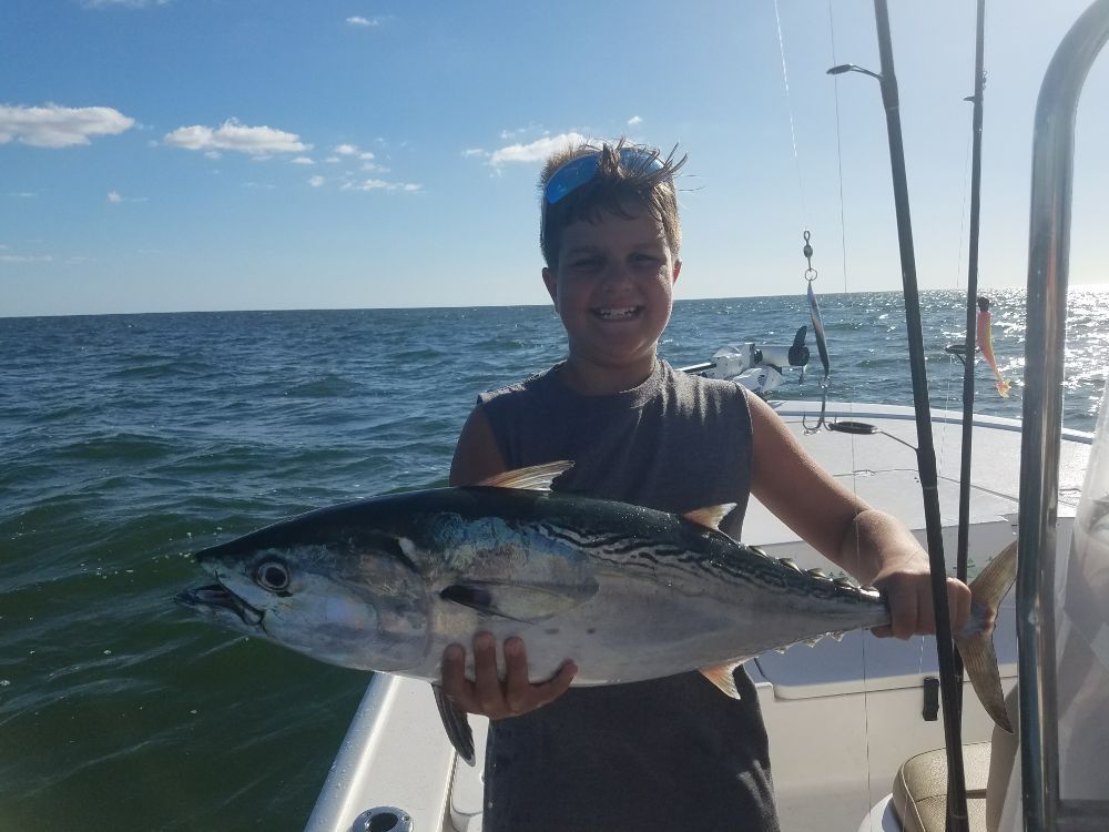 A young boy is holding a large fish on a boat in the ocean.