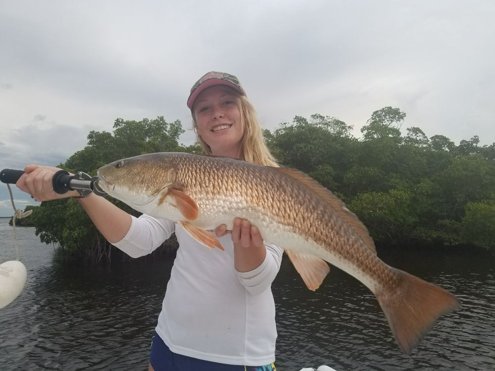 A woman is holding a large redfish in her hands.