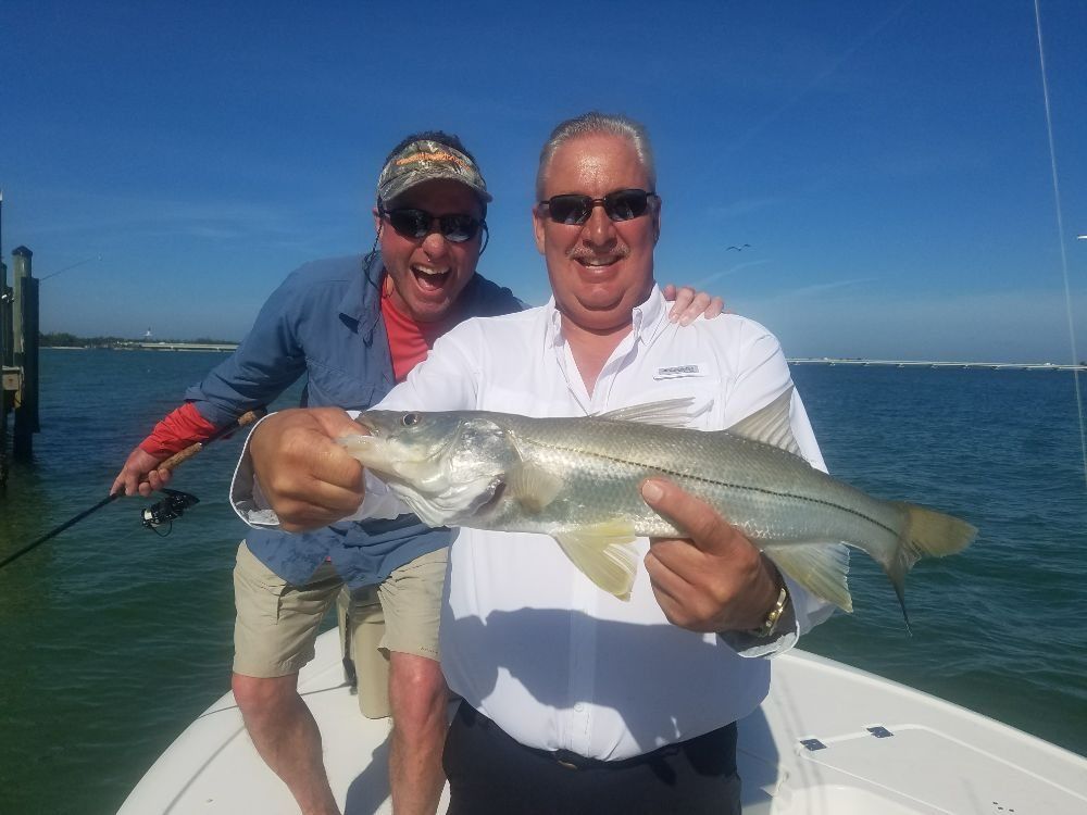 Two men are standing on a boat holding a large fish.
