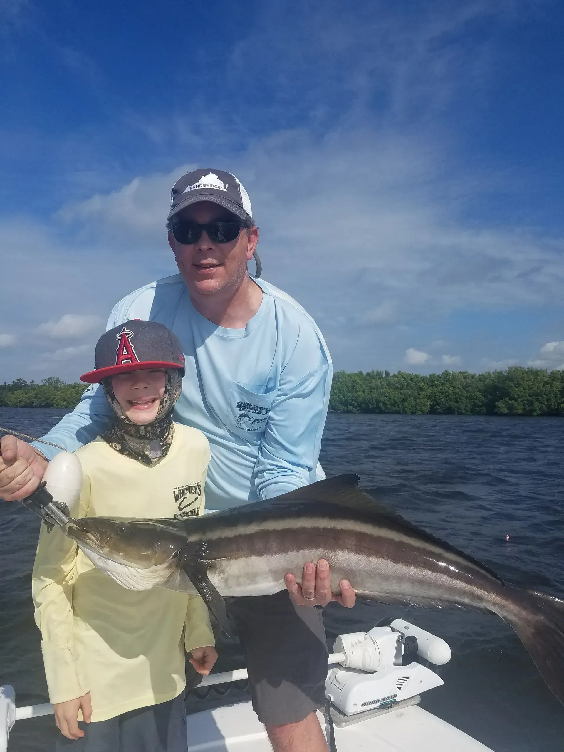 A man and a boy are holding a large fish on a boat.