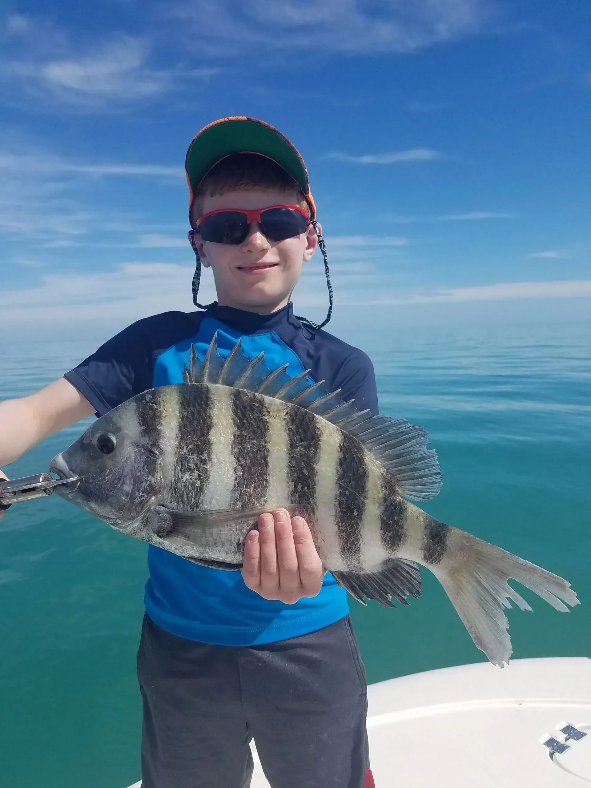 A young boy is holding a large fish in his hands on a boat.