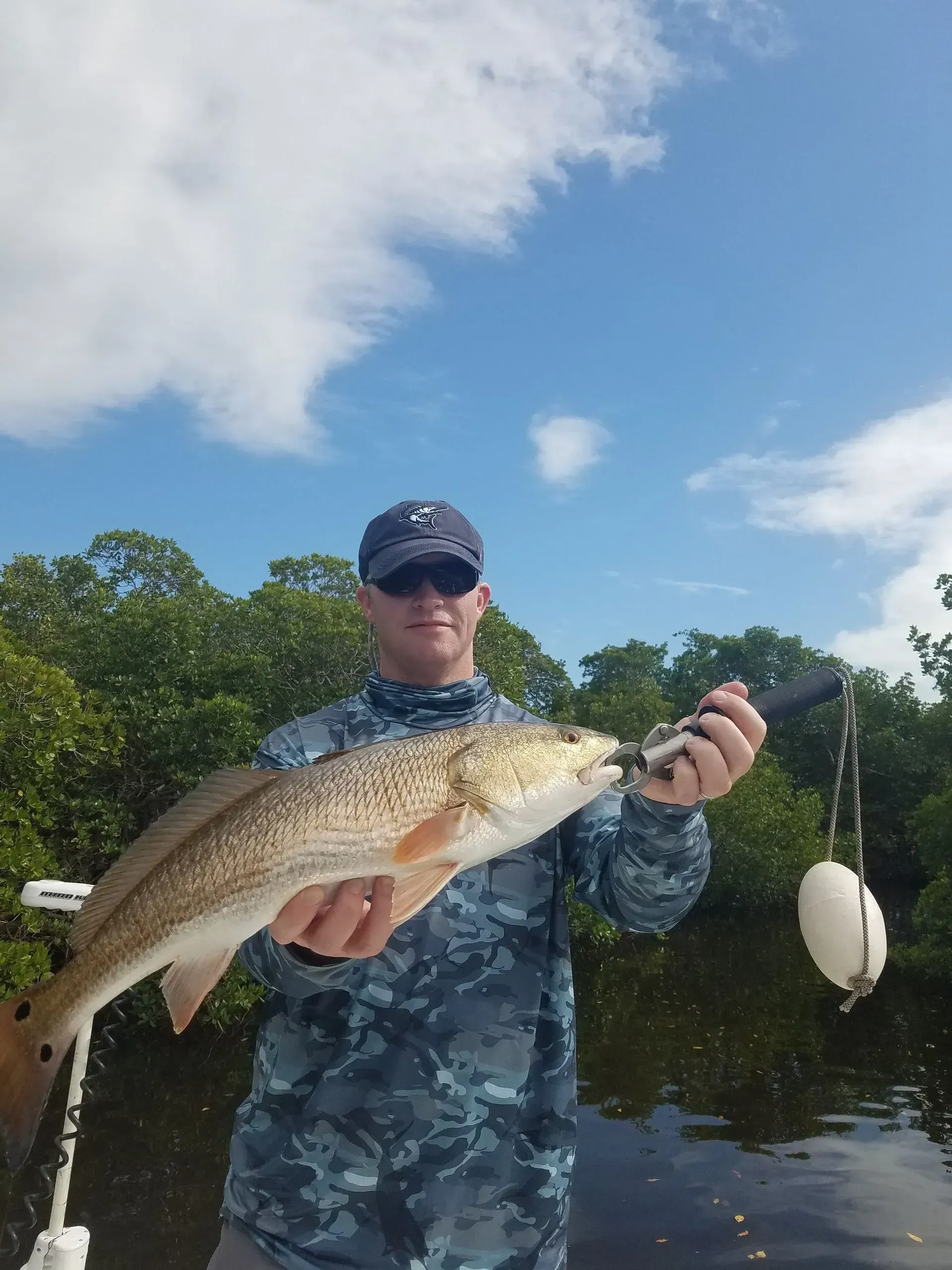 A man is holding a large fish in his hands in front of a body of water.