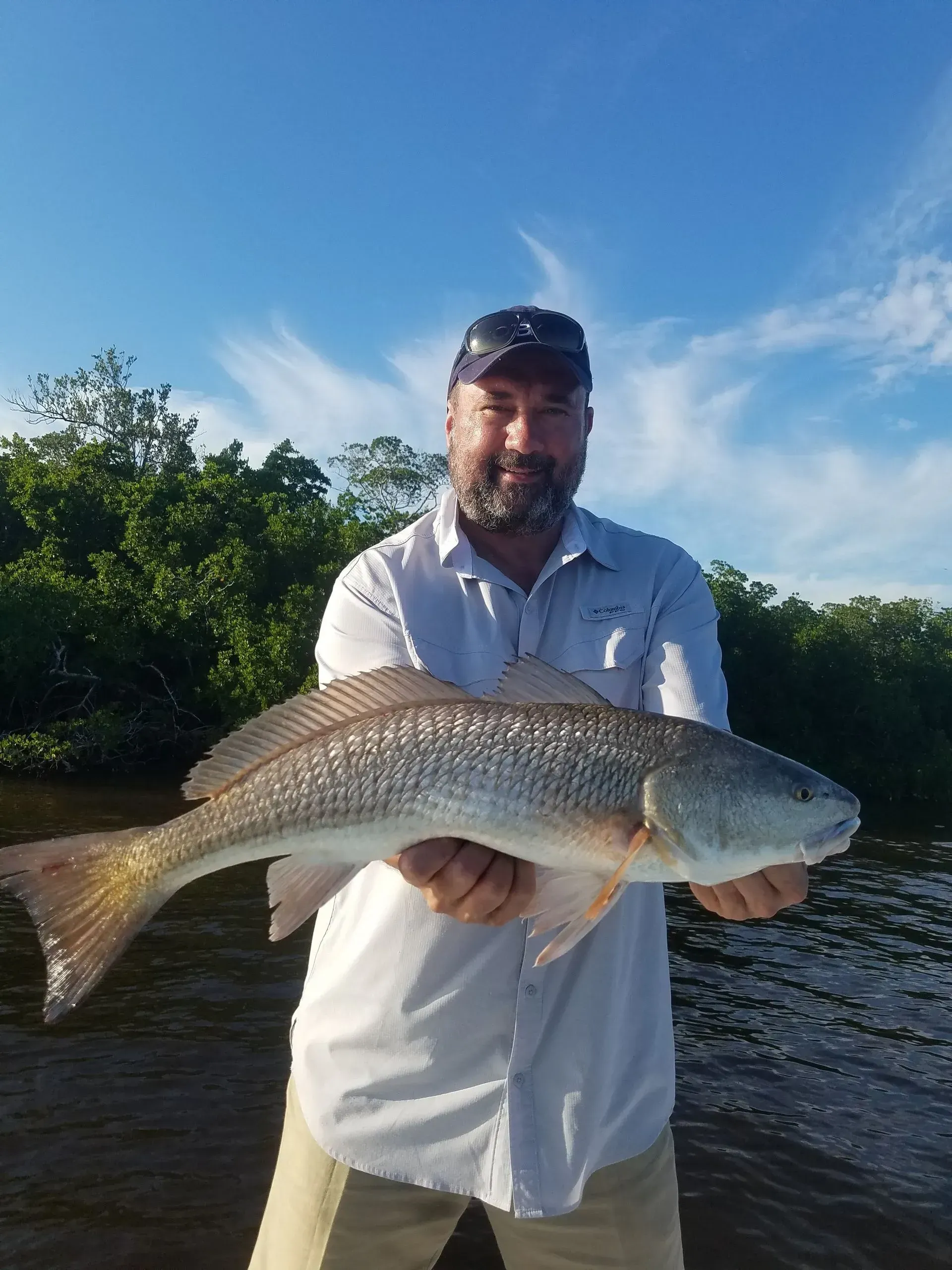A man is holding a large fish in his hands in front of a body of water.