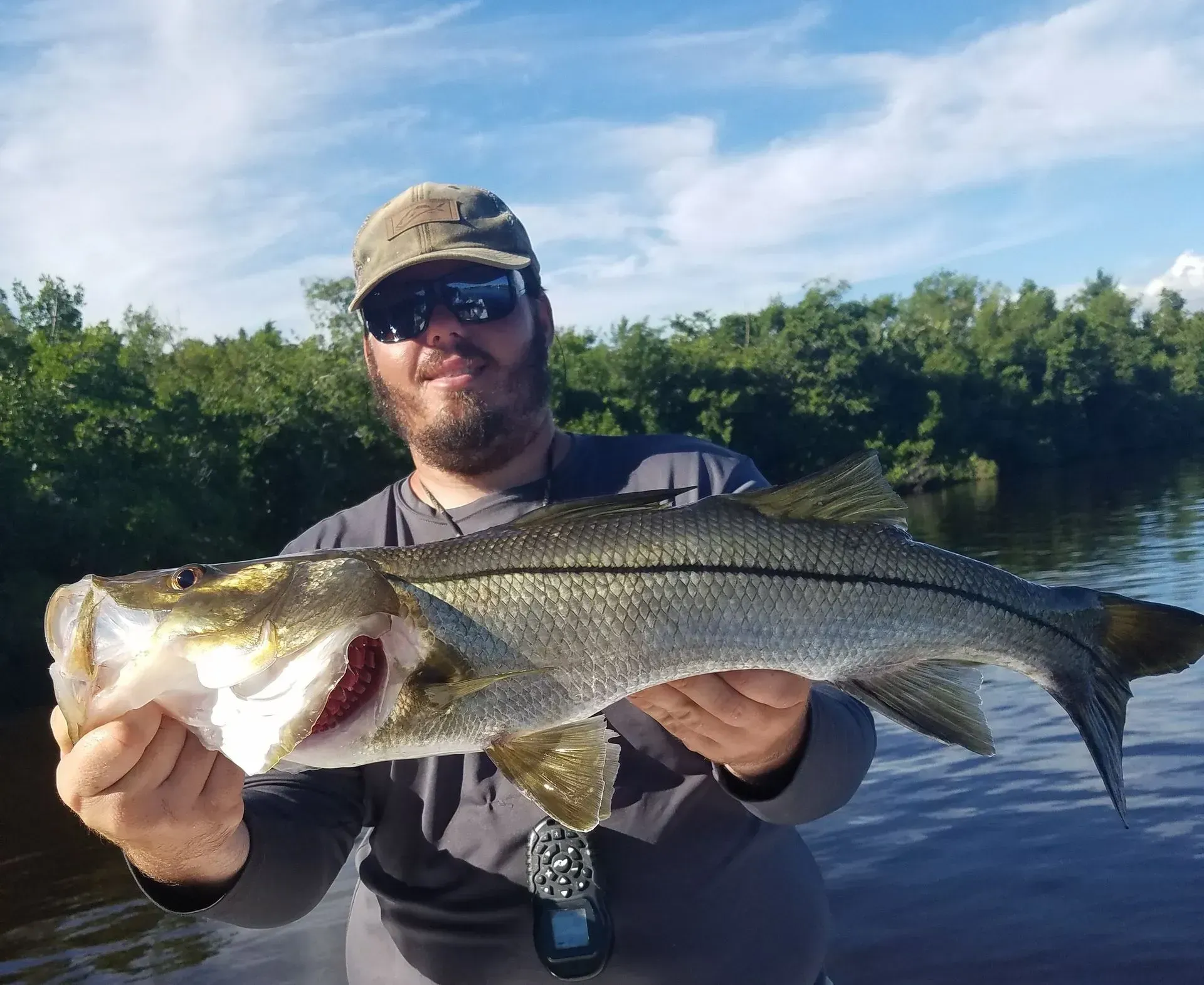 A man is holding a large fish in his hands in front of a body of water.