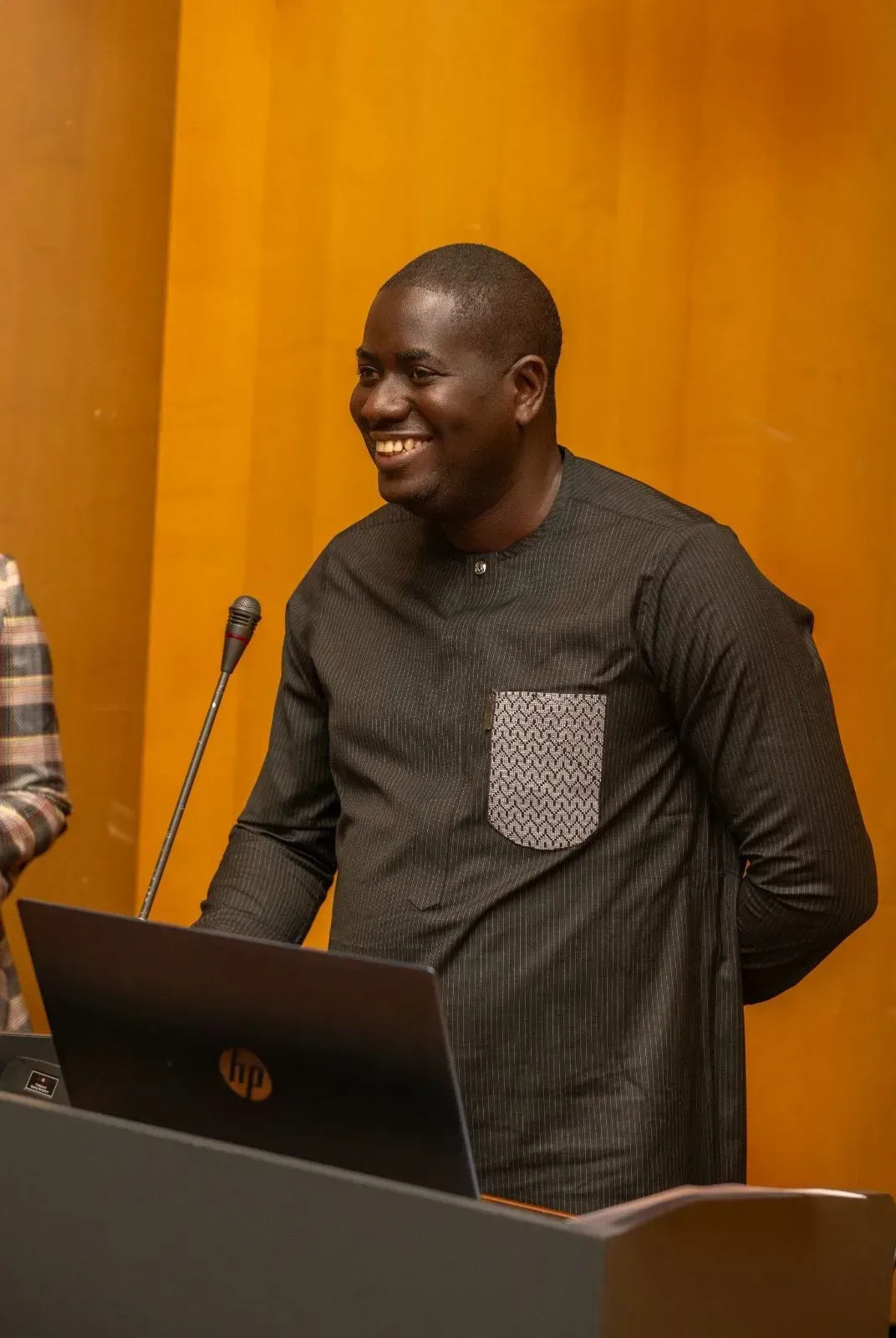 Un homme se tient debout sur un podium avec un ordinateur portable et sourit.