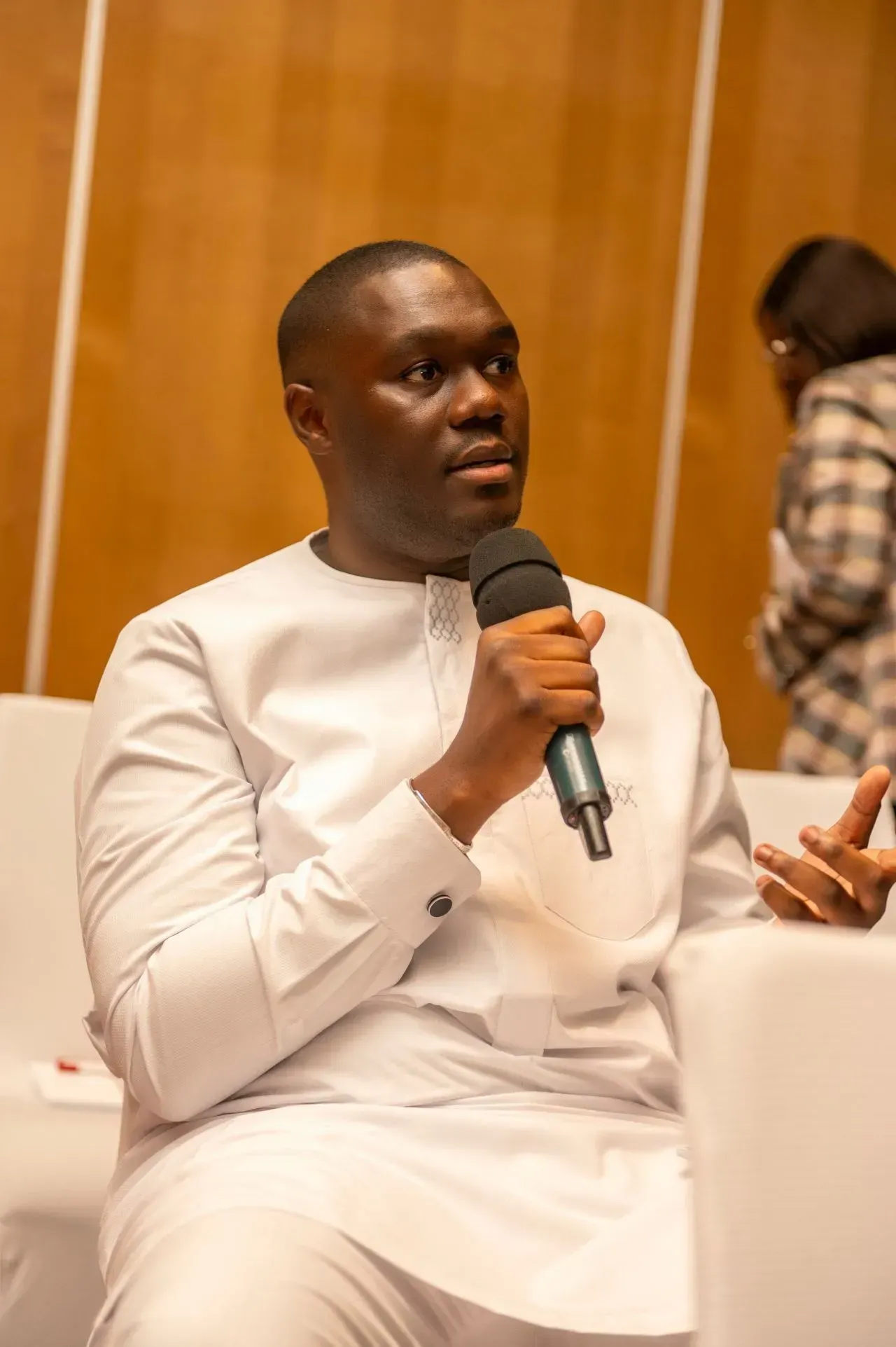 Un homme en chemise blanche tient un microphone et parle dedans.