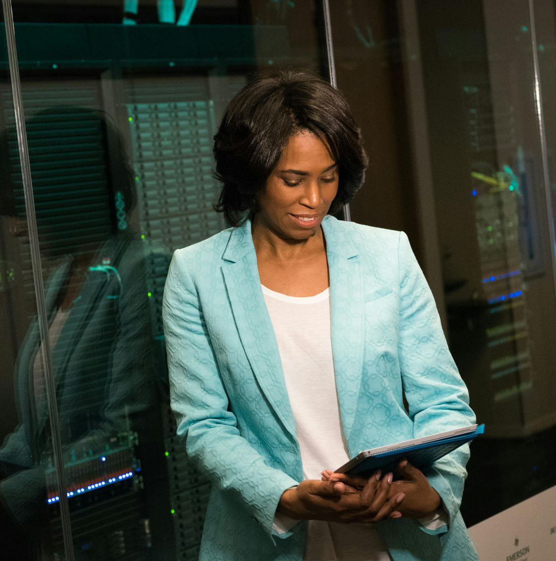 Femme en blazer bleu tenant une tablette devant une salle de serveurs.