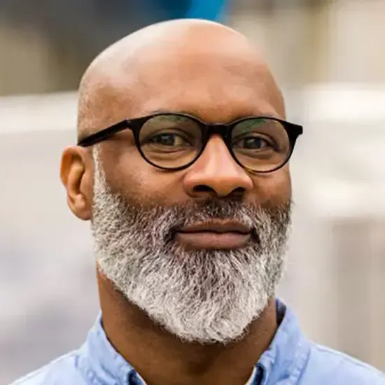 Un homme chauve avec une barbe et des lunettes sourit.