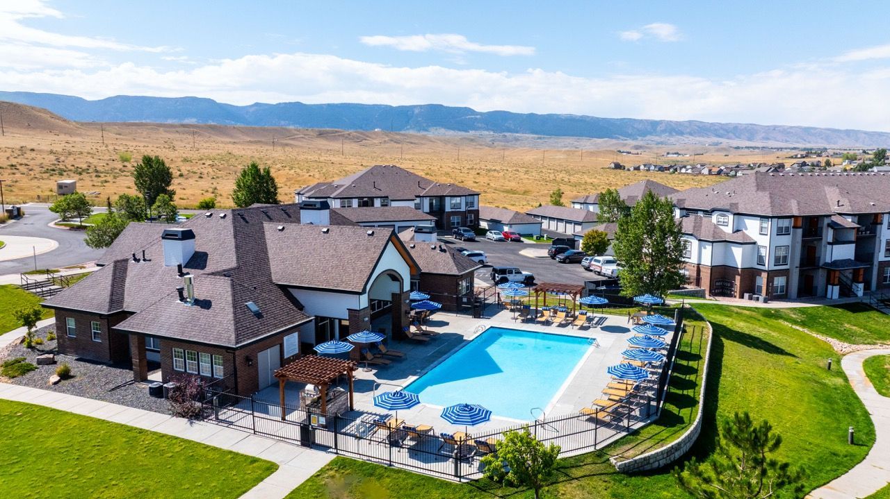 Aerial view of a community pool with lounge chairs and blue umbrellas, surrounded by apartment buildings.