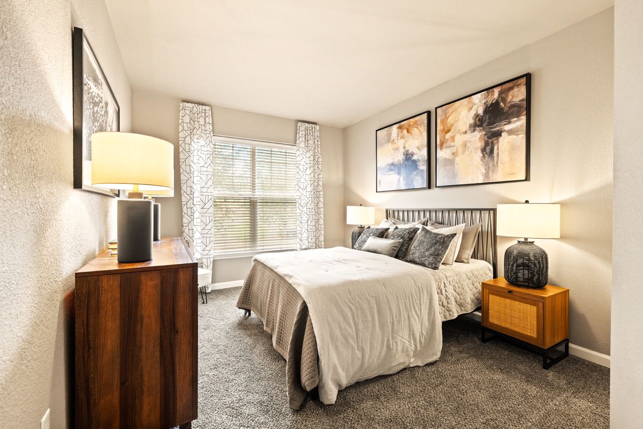 Furnished bedroom with a queen bed, two lamps, nightstands, and abstract wall art.