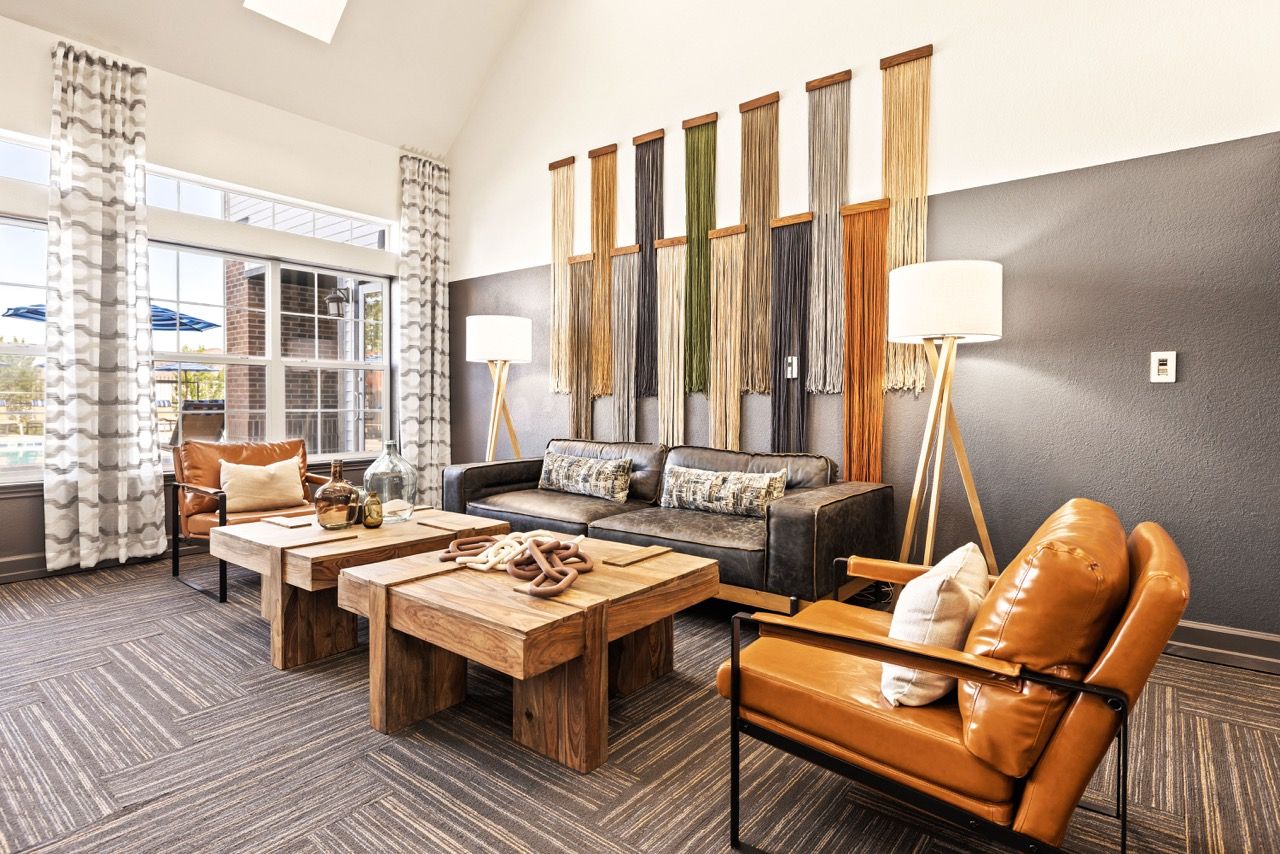 Contemporary apartment community lounge with leather seating, wooden coffee tables, and large windows.