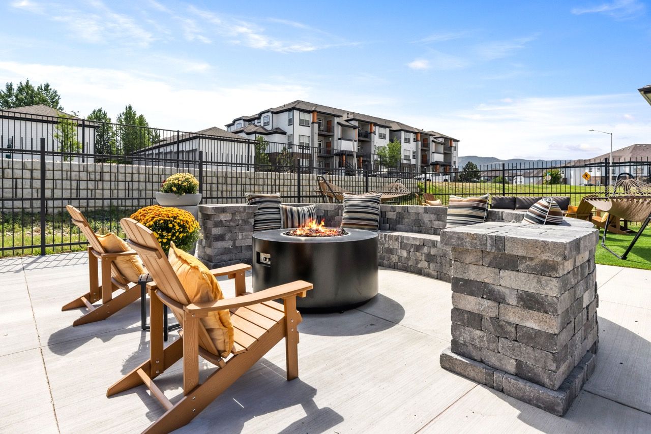 Outdoor communal patio with a circular fire pit, cushioned lounge chairs, and stacked stone seating.