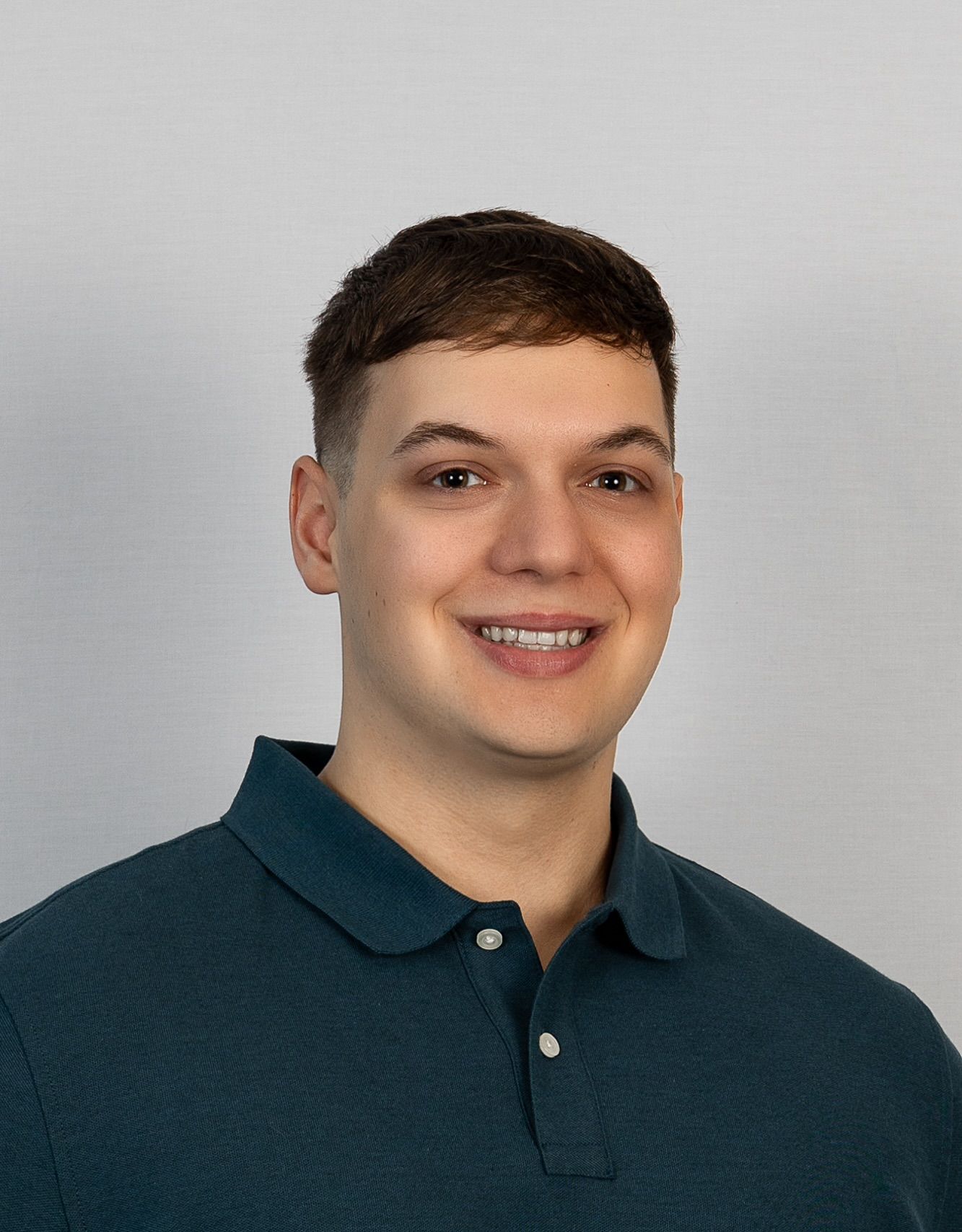 A young man wearing a blue polo shirt is smiling for the camera.