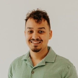 Smiling man with brown hair and a small beard in a green shirt, standing indoors.