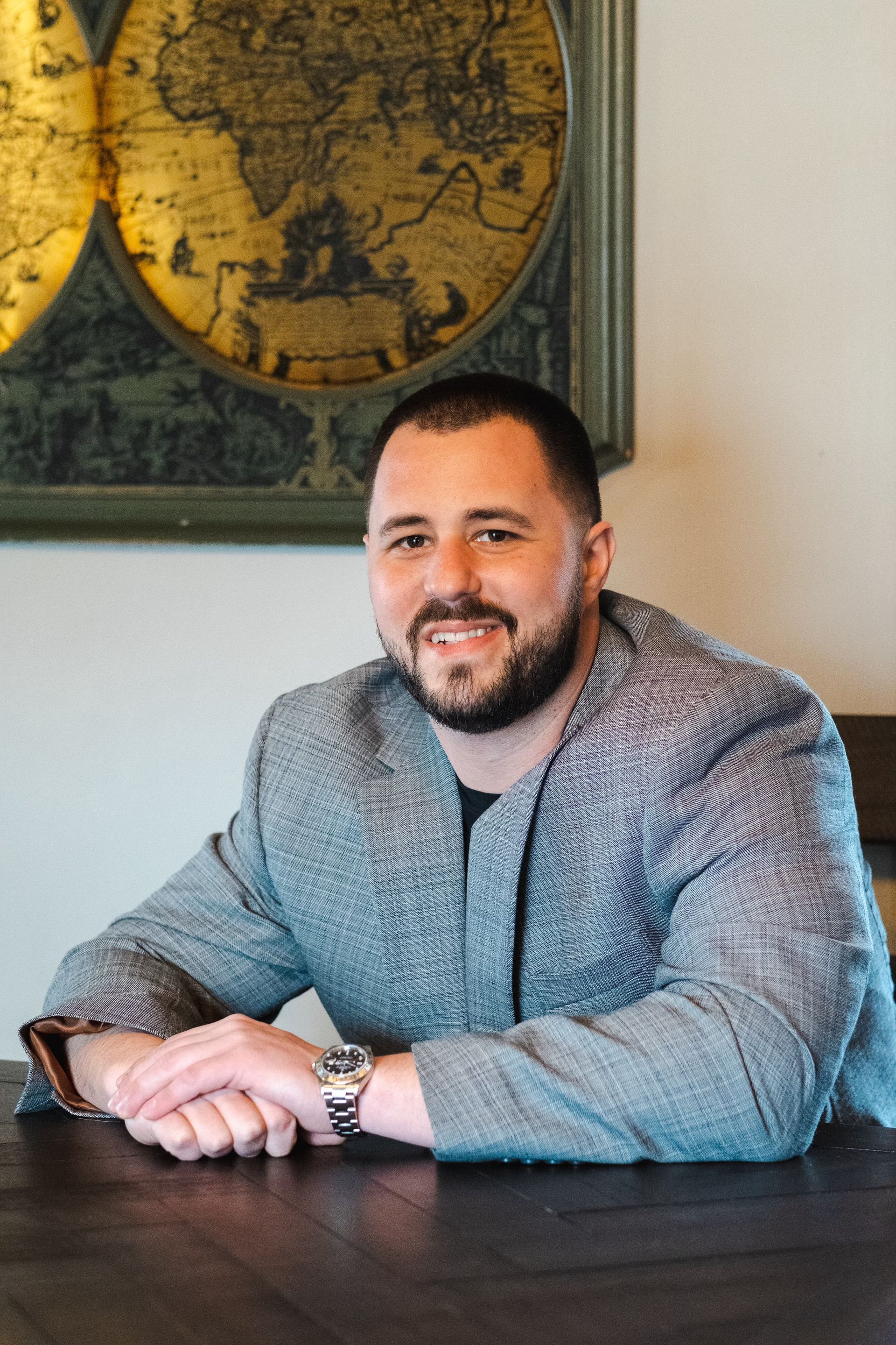 A man with a beard is sitting at a table with his hands folded.