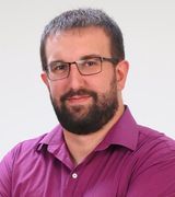 A man with a beard and glasses is wearing a purple shirt.
